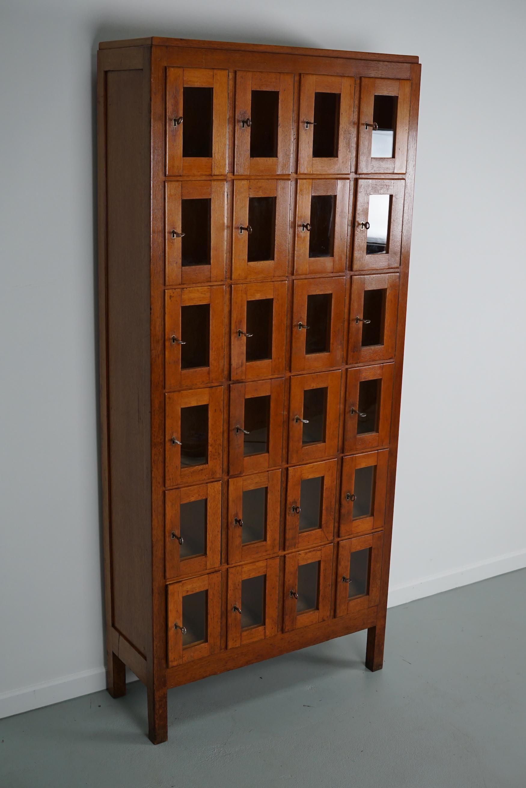 This vintage Dutch oak locker with glass doors was made around the 1930s in the Netherlands. It was used on an army base to store the headphones for the tank drivers and pilots during WW2. Every door has its own individual key. The interior