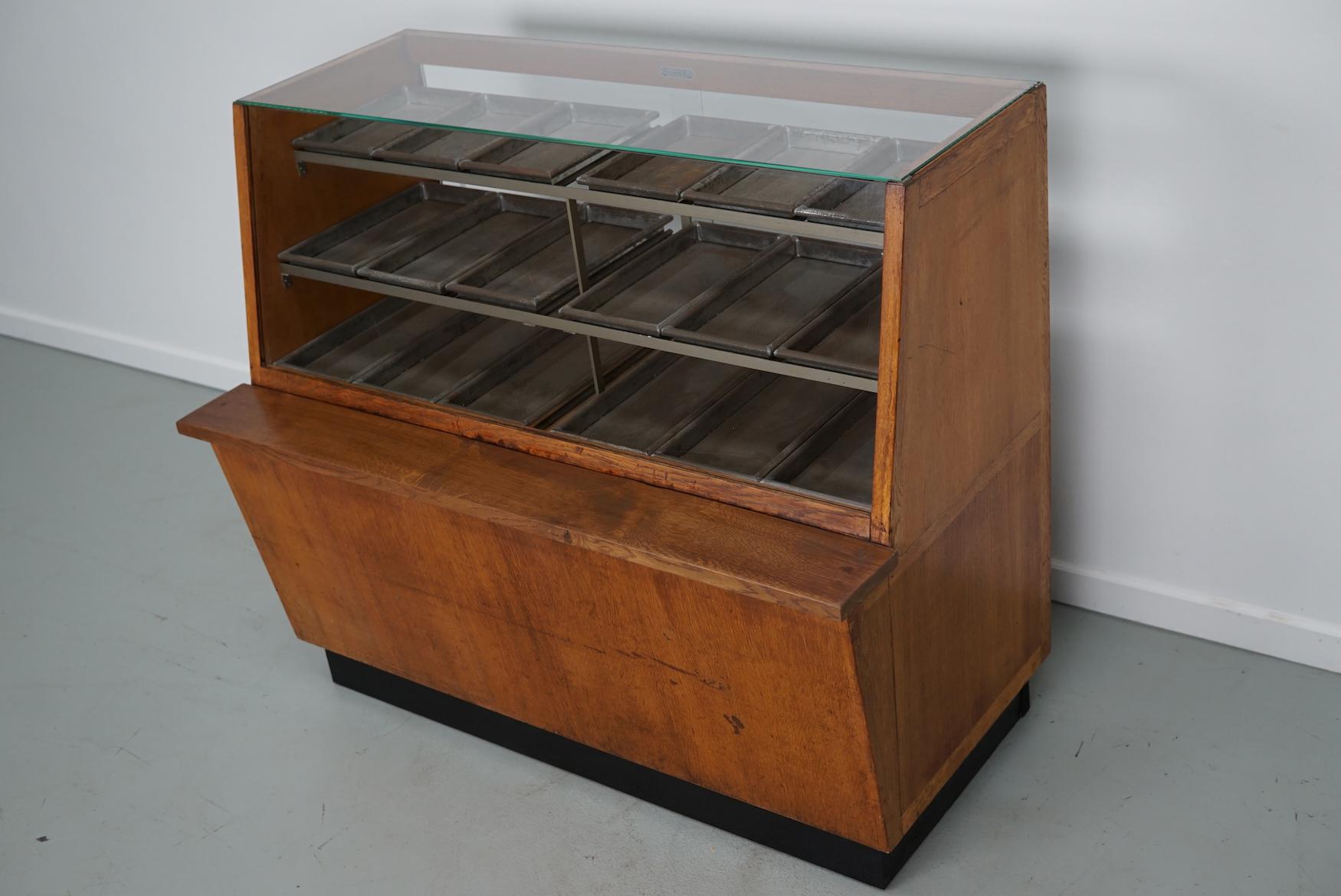 This vintage haberdashery shop counter dates from the 1950s and was made in the Netherlands. It features a wooden frame, glass casing and metal drawers / trays in different sizes D 21 / 28 / 35 x W 13 x H 2.5 cm. 