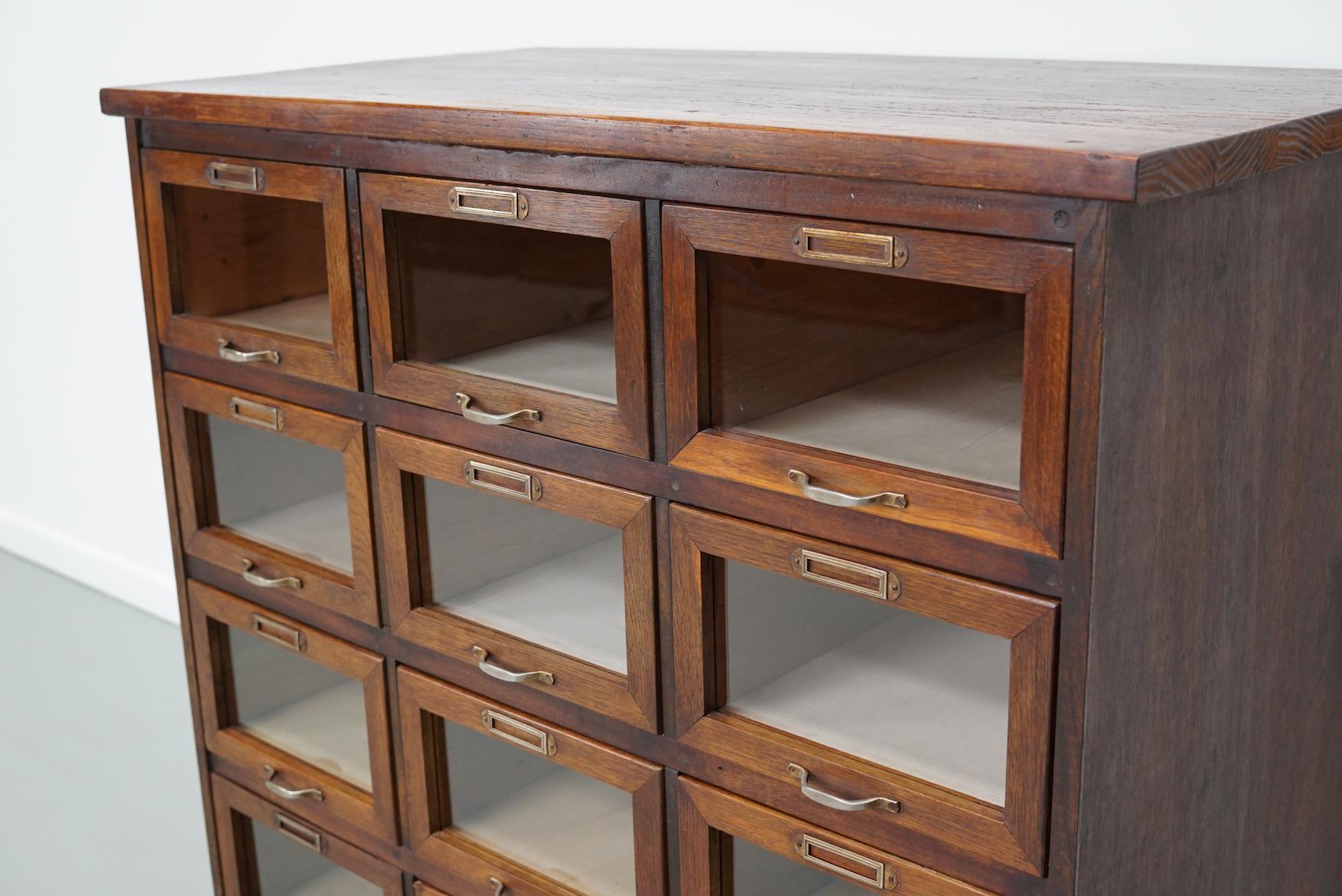Questo mobile da merceria è stato prodotto negli anni '1950 nei Paesi Bassi. Dispone di 12 cassetti in Oak con frontali in vetro e ferramenta in metallo. In origine era un magazzino di biancheria intima. La struttura in legno è stata realizzata in