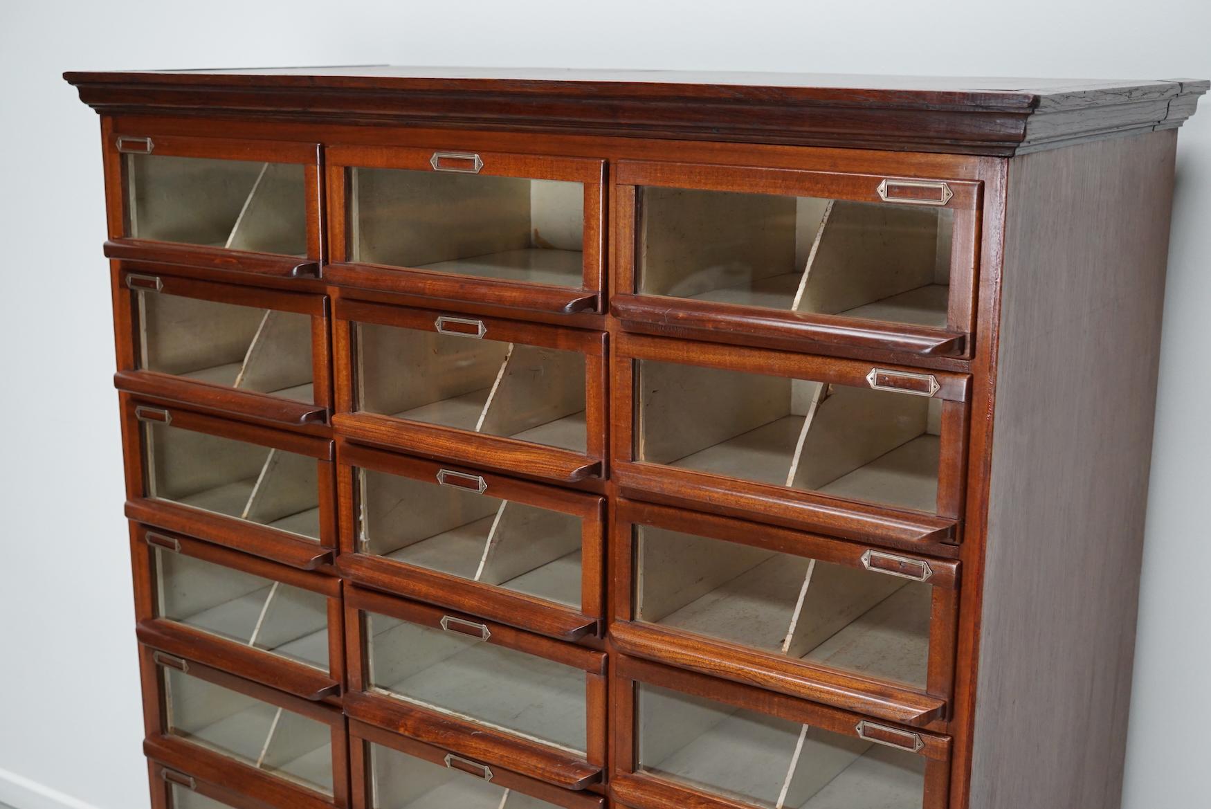 This haberdashery cabinet was produced during the 1930s in the Netherlands. This piece features 24 paper covered drawers in mahogany with mostly original glass fronts, mahogany handles and name card holders. It was originally used in a shop for
