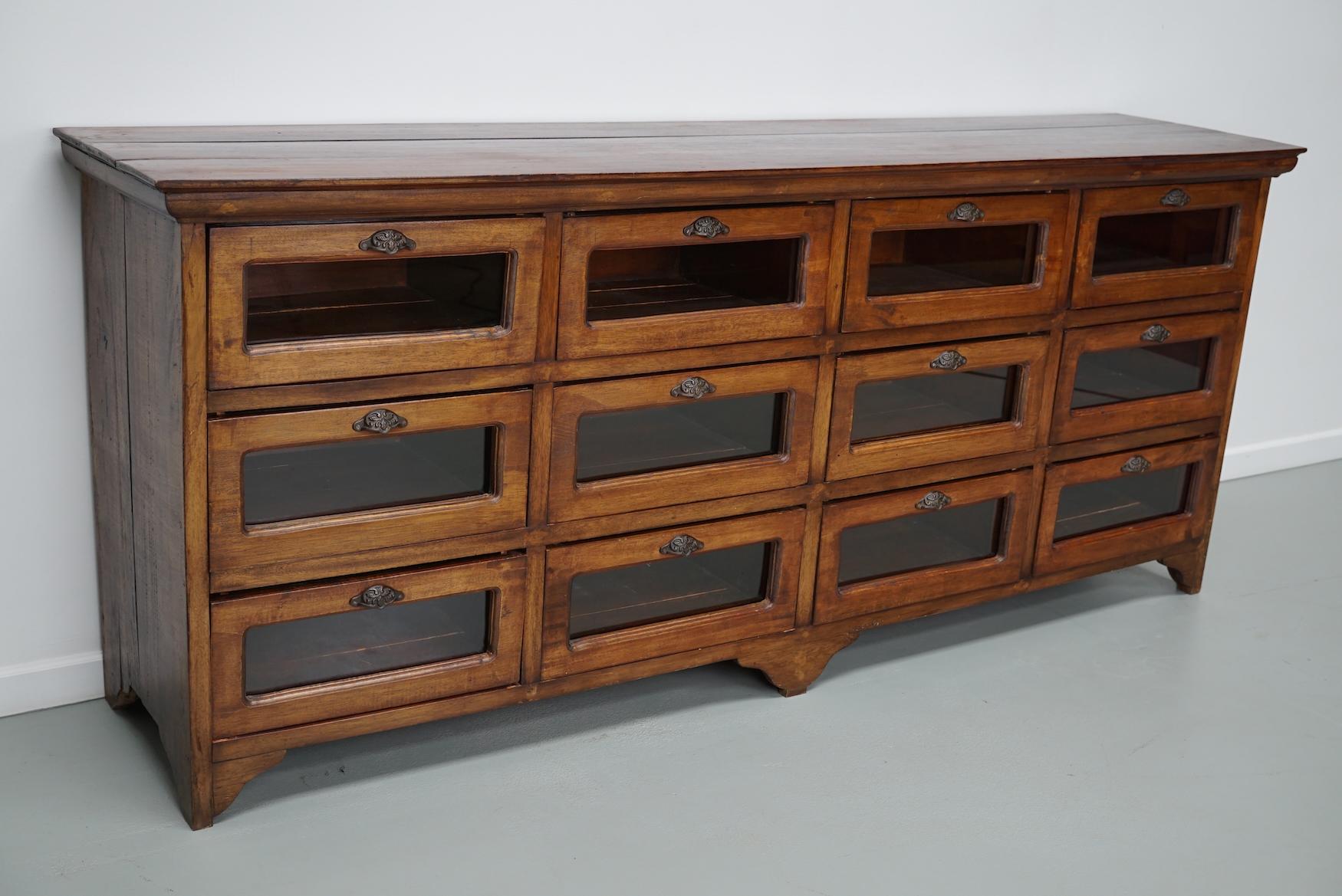 This vintage haberdashery cabinet was produced in the second half of the 20th century in Indonesia. It features 12 large drawers in teak with glass fronts and cast iron handles. The interior dimensions of the drawers are: DWH 34 x 40 x 17 cm.