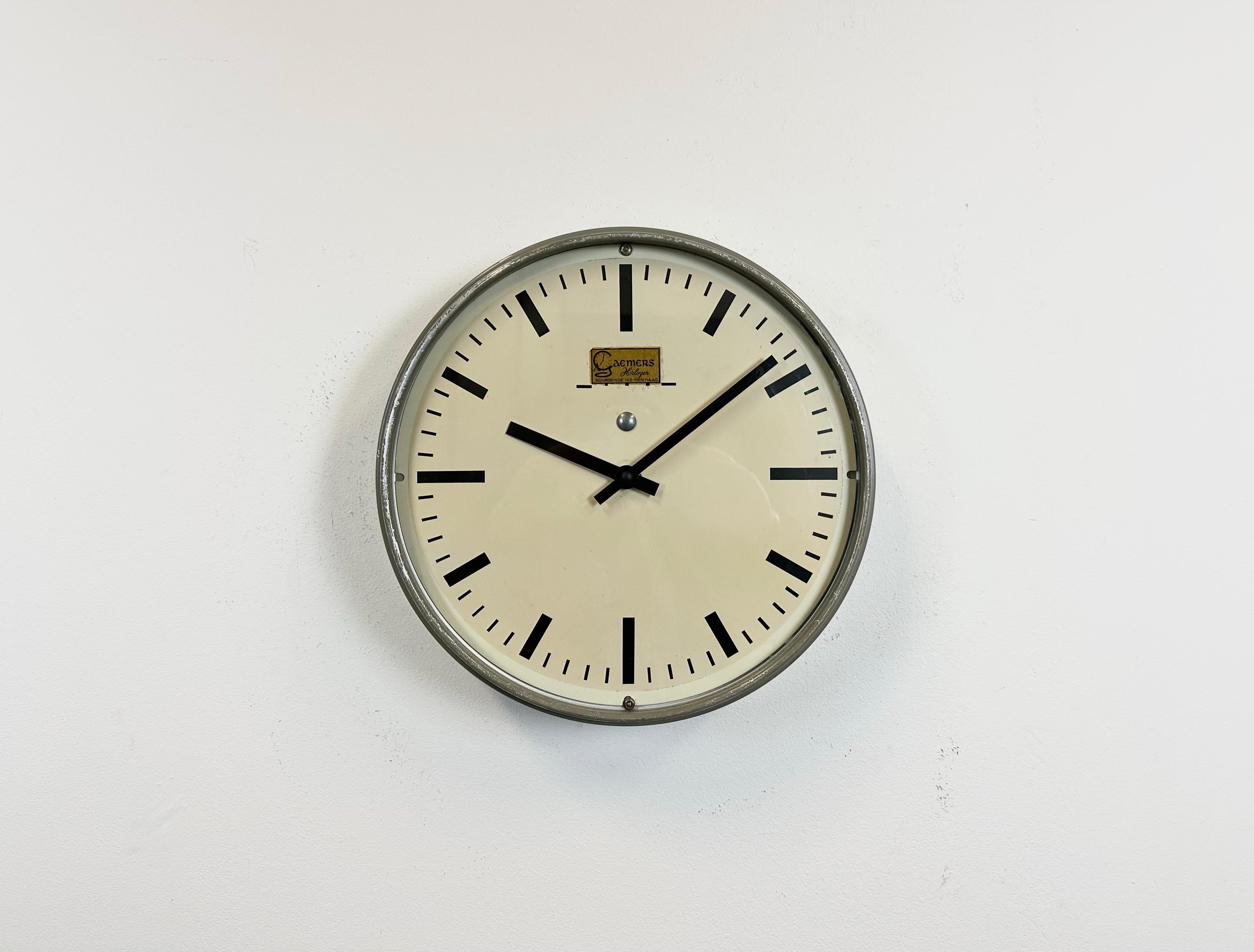 This wall clock was produced by Gaemers Horloger Den Haag in Netherlands during the 1950s. It features a metal frame, iron dial, aluminium hands and a clear glass cover. The piece has been converted into a battery-powered clockwork and requires only