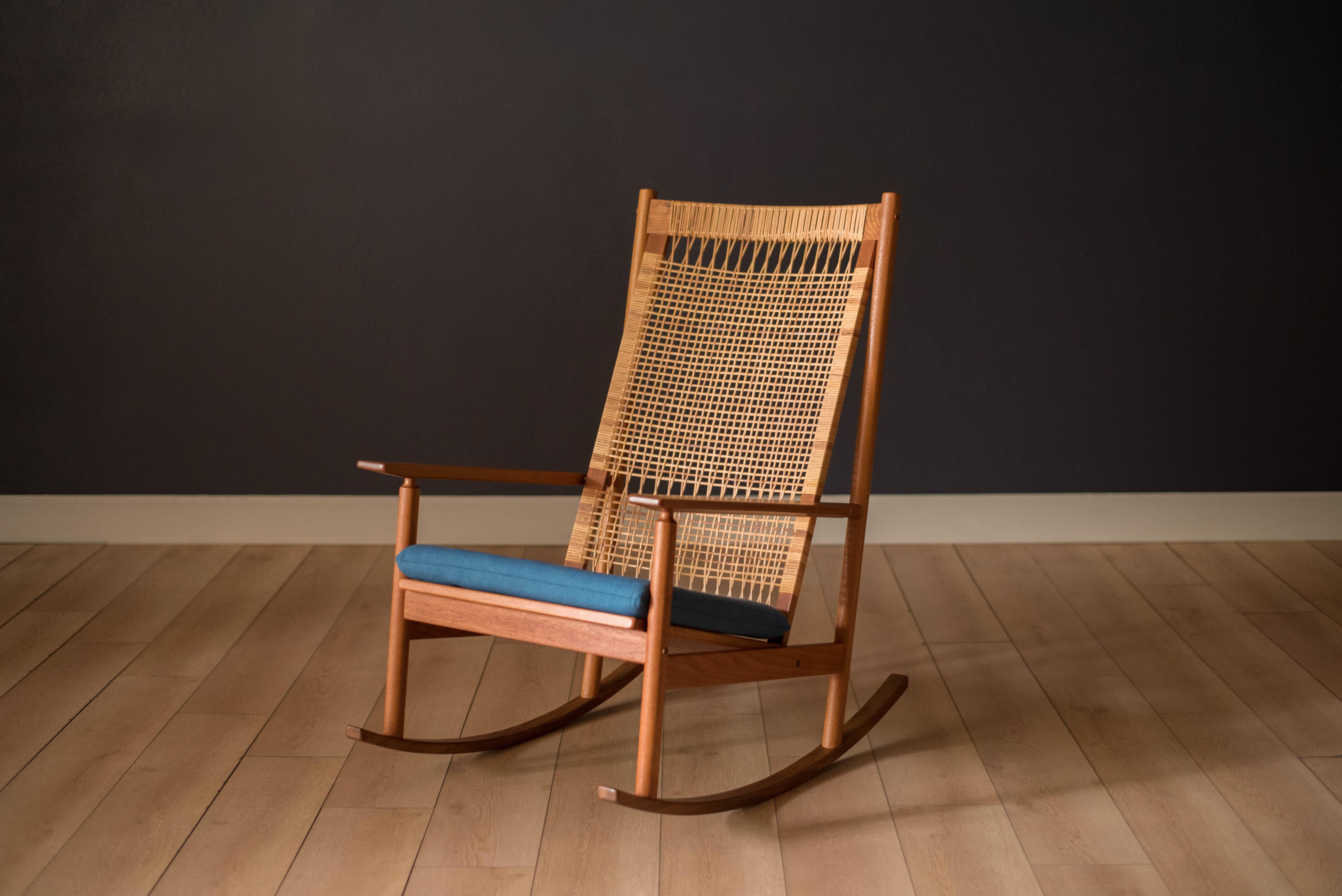 Mid-Century Modern DUX rocking armchair designed by Hans Olsen for Juul Kristensen, circa 1960's. This piece features a natural cane tall backrest with sculpted teak and brass details. The seat cushion has been reupholstered in a blue tweed
