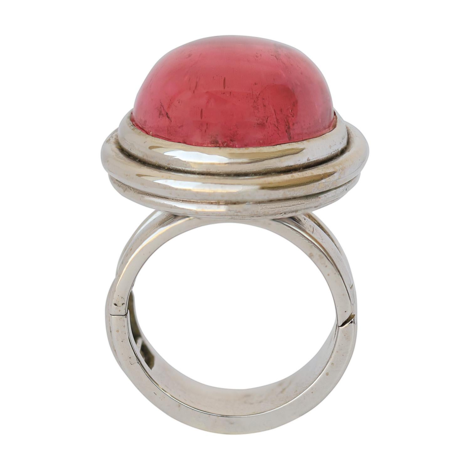 A stunning, generously sized oval-shaped cabochon pink tourmaline, weighing around 30 carats, graces this ring. It is elegantly nestled within a two-tier bezel setting, featuring a delicate flower petal pattern on the under gallery. Crafted with