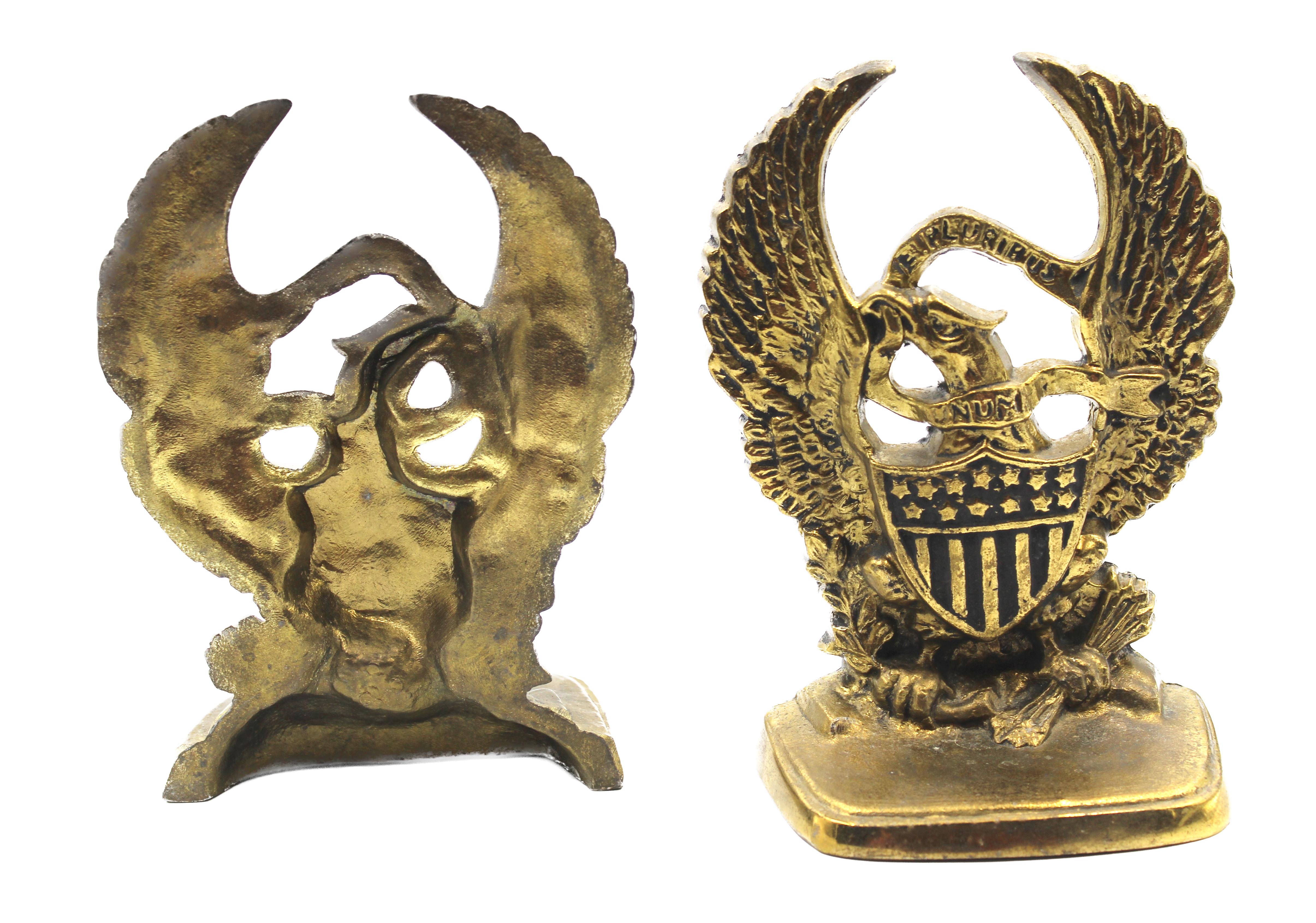 Offered is a vintage set of brass bookends featuring an eagle with widely spread wings. The eagle holds arrows in its talons and appears with a large shield against its chest. The eagle carries a banner in its mouth that reads 