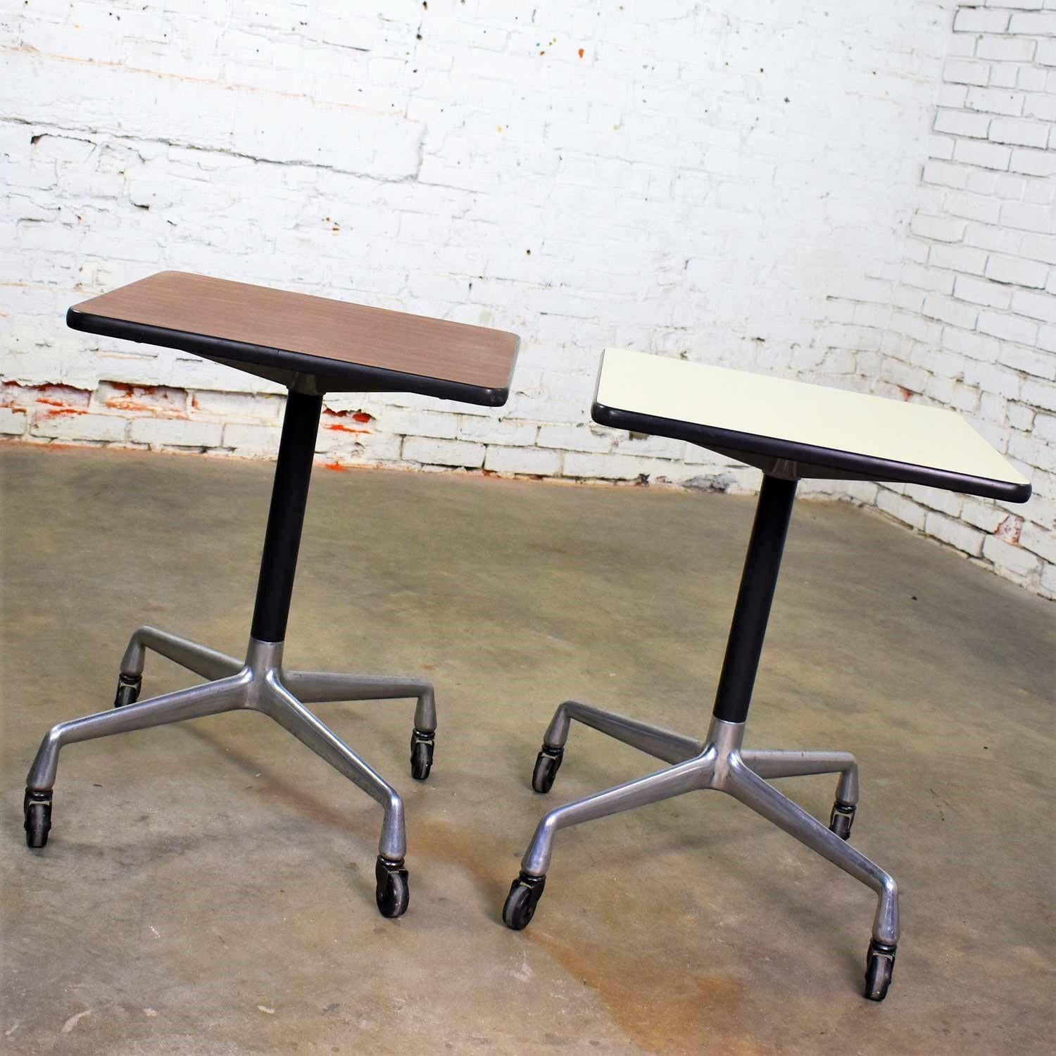 Two handsome square rolling side tables designed by Charles and Ray Eames for Herman Miller. Both with universal bases. One has a white laminate top and one has a faux wood grain laminate top. Each is in wonderful vintage condition with the normal