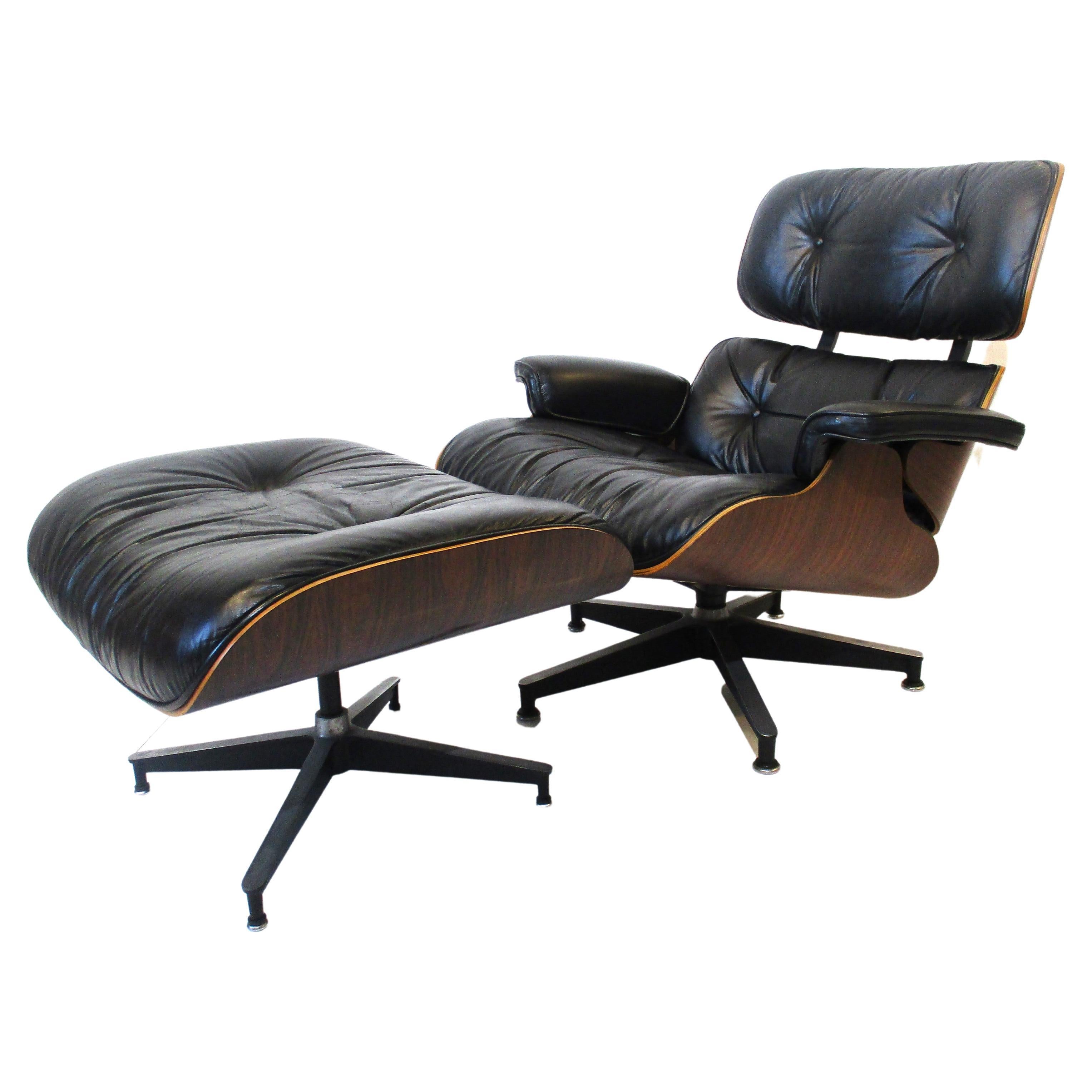 Un fauteuil Eames 670 et un ottoman 671 en palissandre brésilien foncé, recouvert d'un cuir noir doux et lisse. La chaise repose sur une base en étoile pivotante en fonte d'aluminium avec des coussinets et le pouf est non pivotant sur sa base en