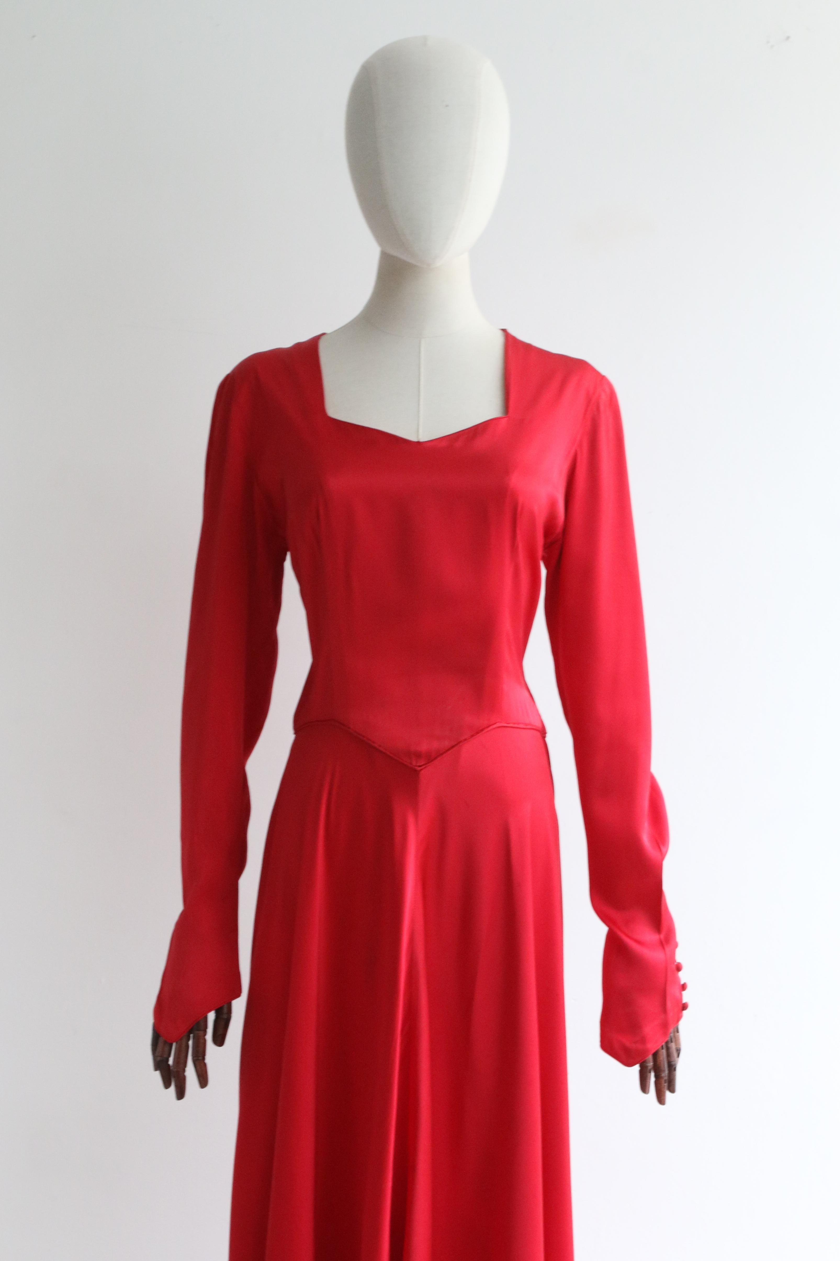 This breathtaking early 1940's crimson satin dress, rendered in a full circle cut and tailored to perfection, is the perfect piece for that special occasion.  

The V shaped neckline is framed by a simple shoulder line, accented by internally sewn