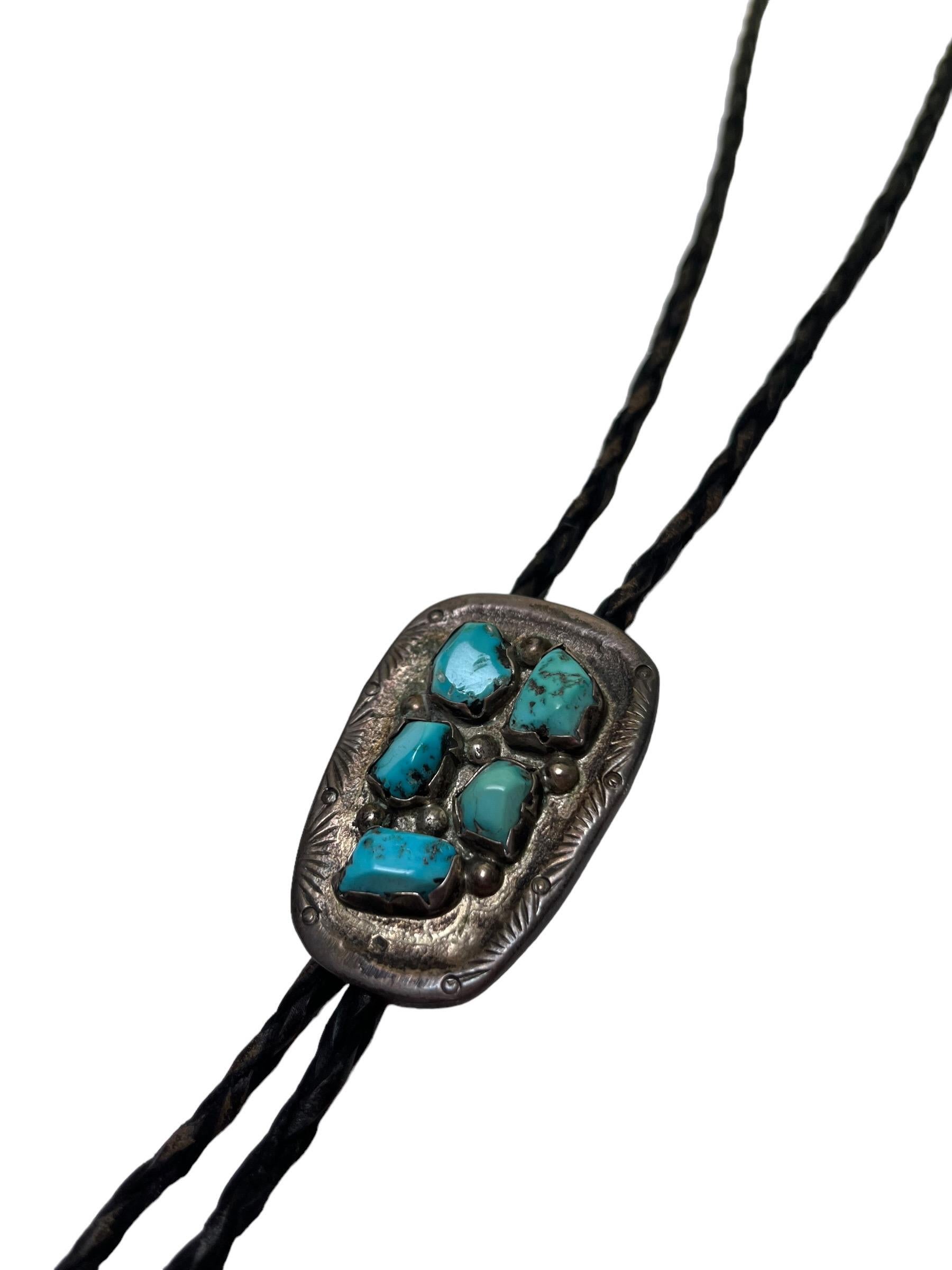 Vintage 1960s Native American Navajo Turquoise, Silver. & Leather Bolo Tie

This gorgeous peice features five beautiful turquoise nuggets in varying shades which are inlaid atop a stamped silver medallion. The piece is unmarked aside from the