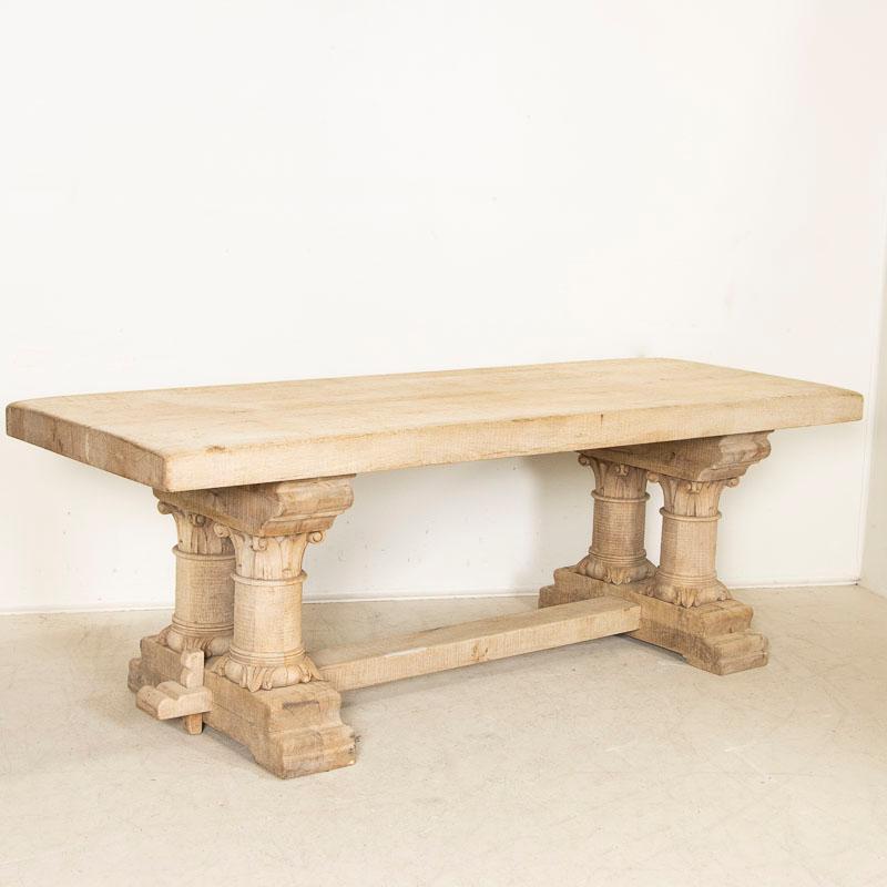 This bleached oak table has powerful presence thanks to the heavy carved columns that create the visually stunning legs of the large trestle base. The massive 3