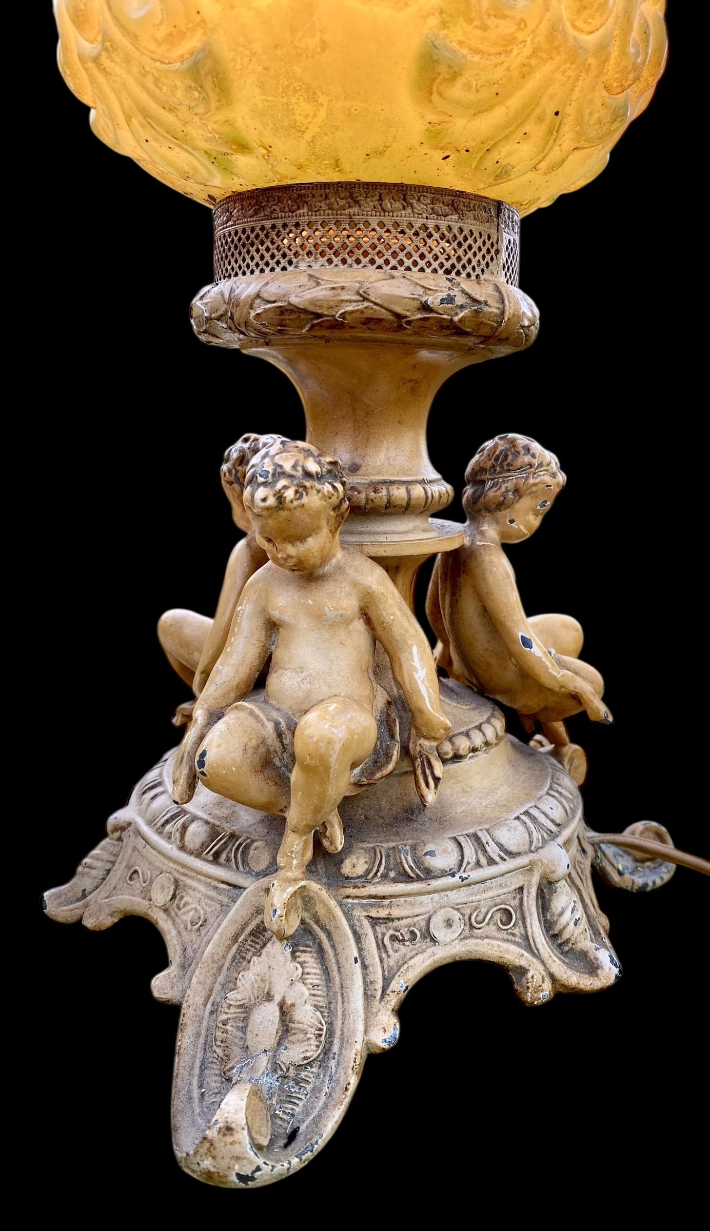 Questa lampada dei primi del Novecento presenta tre bambini, o cherubini, in uno stile che imita una statua del primo Rinascimento italiano. Il bellissimo paralume in vetro colorato e lavorato a mano, con tre volti di cherubini e una lavorazione a