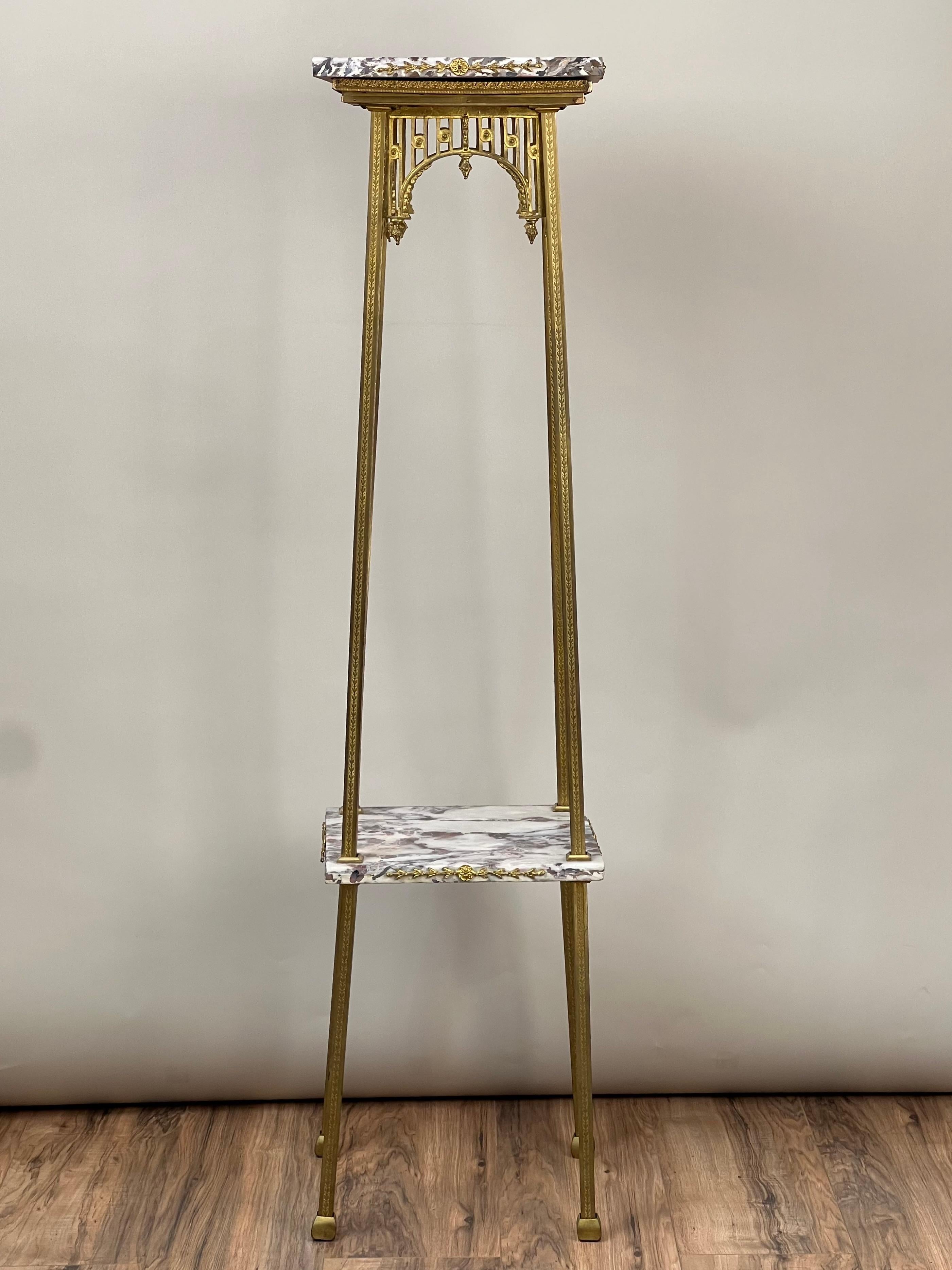 This elegant Louis XV style two-tier plant stand from the early 20th century showcases the timeless beauty of brass and marble craftsmanship. The stand features an ornate brass frame with delicate detailing, supporting two tiers of beautifully