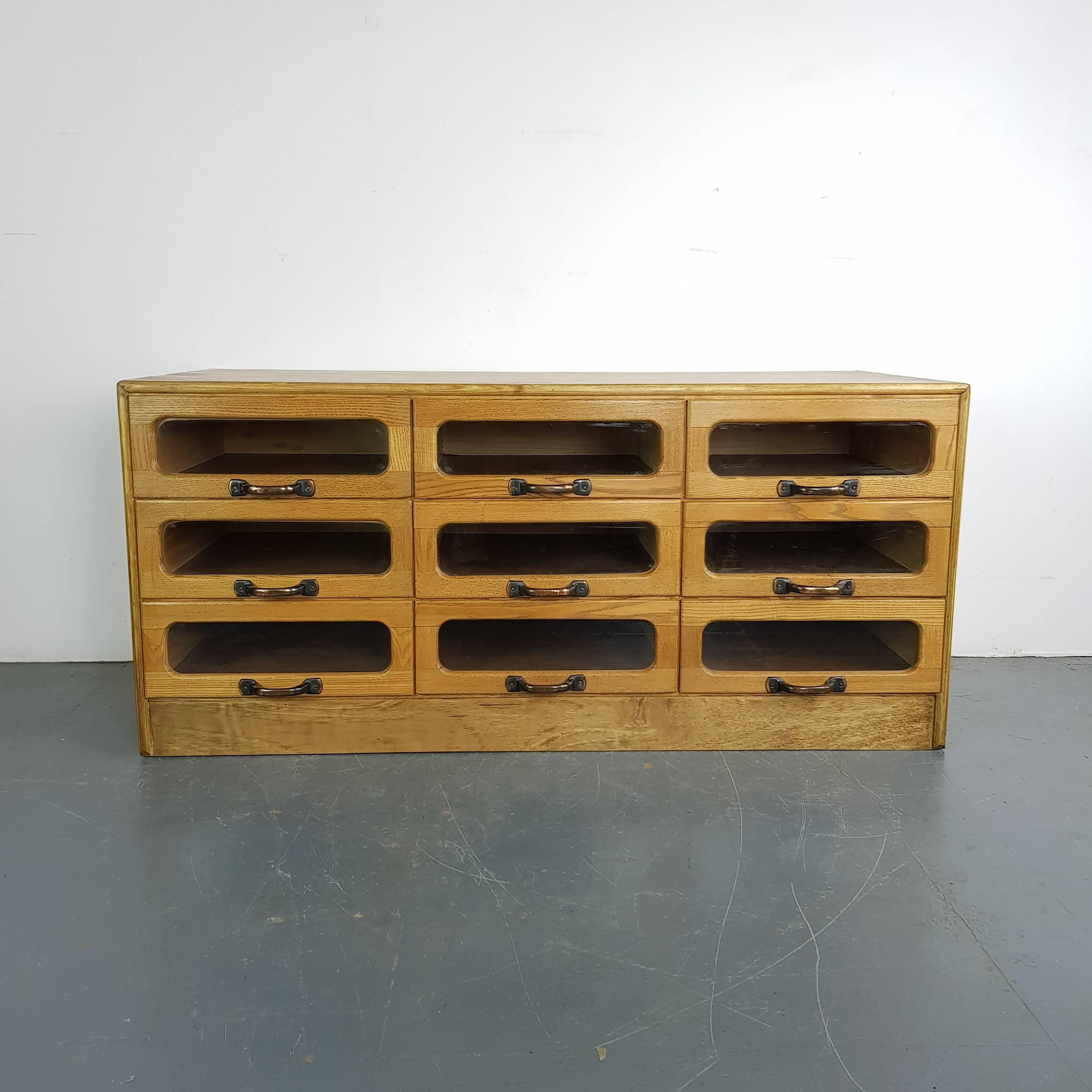 Nine drawer haberdashery shop cabinet from the first half of the last century. 

It has nine glass fronted drawers, all with metal D handles. The right height for standing stuff on - a TV or record player or some pictures.

Approximate