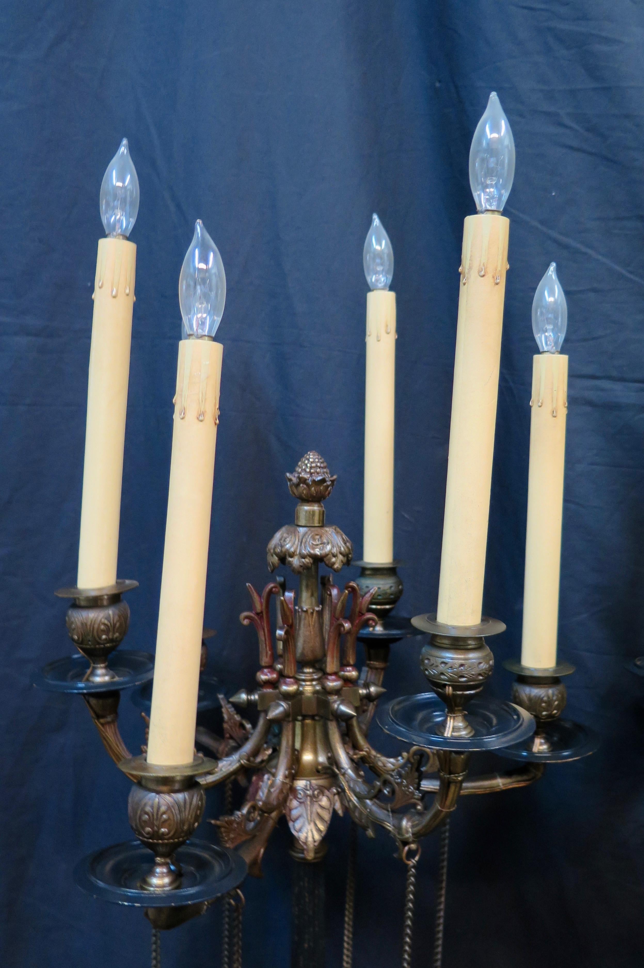 These vintage Edwardian designed tall bronze candelabra lamps are elegantly decorated with a stylish blackened columns and matching bobeche accents. Each six light lamp features extended curved candlestick arms festooned with chaining. Sturdy bronze