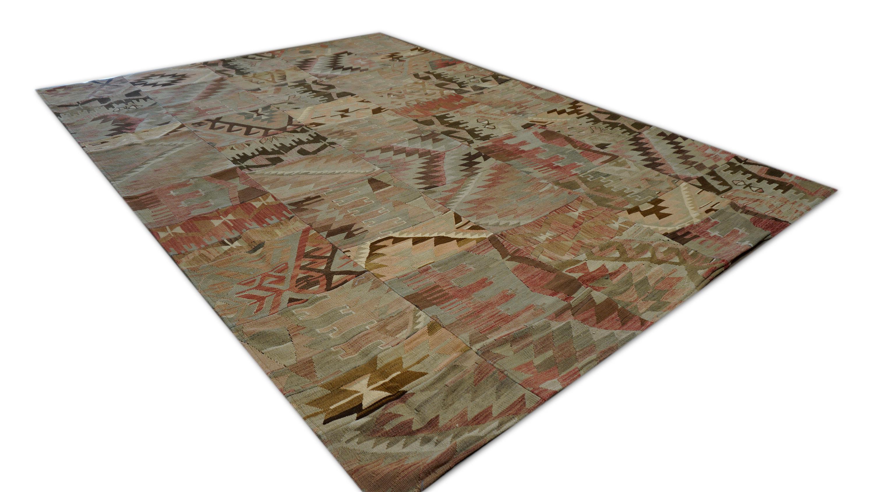 This hand-woven wool rug is an authentic patchwork composition crafted from vintage fragments, each featuring bold tribal motifs and geometric patterns. The multicolored palette blends muted earth tones with soft pink, brown, and tan, giving the