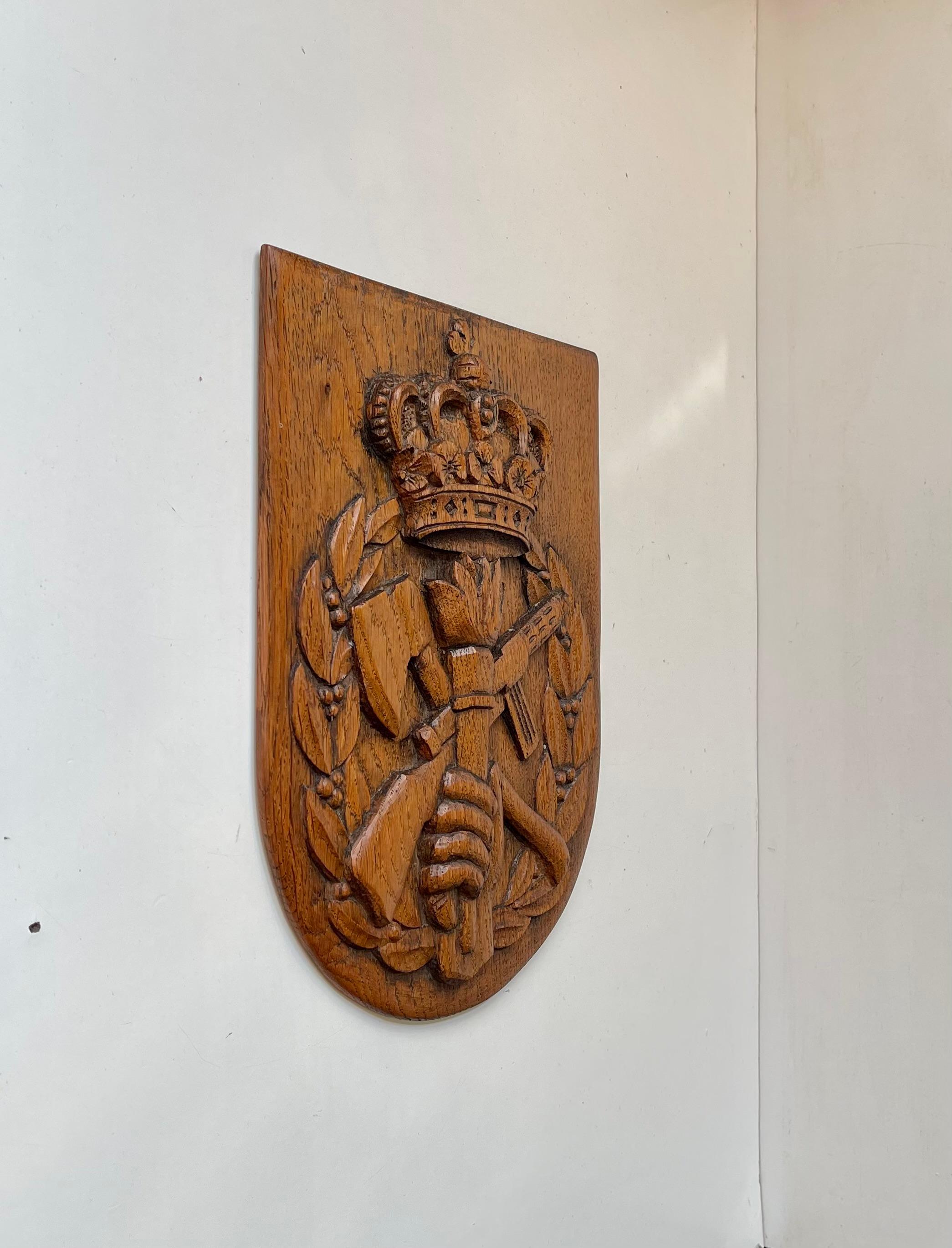 Unusual East Block/Balkan Coat of Arms in hand-carved oak. An excess of masculine elements: crown, machine-gun, torch, axe, fist. Heraldic symbolism here and there. Very wellkept - can be displayed on the wall. Measurements: H: 29.5 cm, W: 23, Dept: