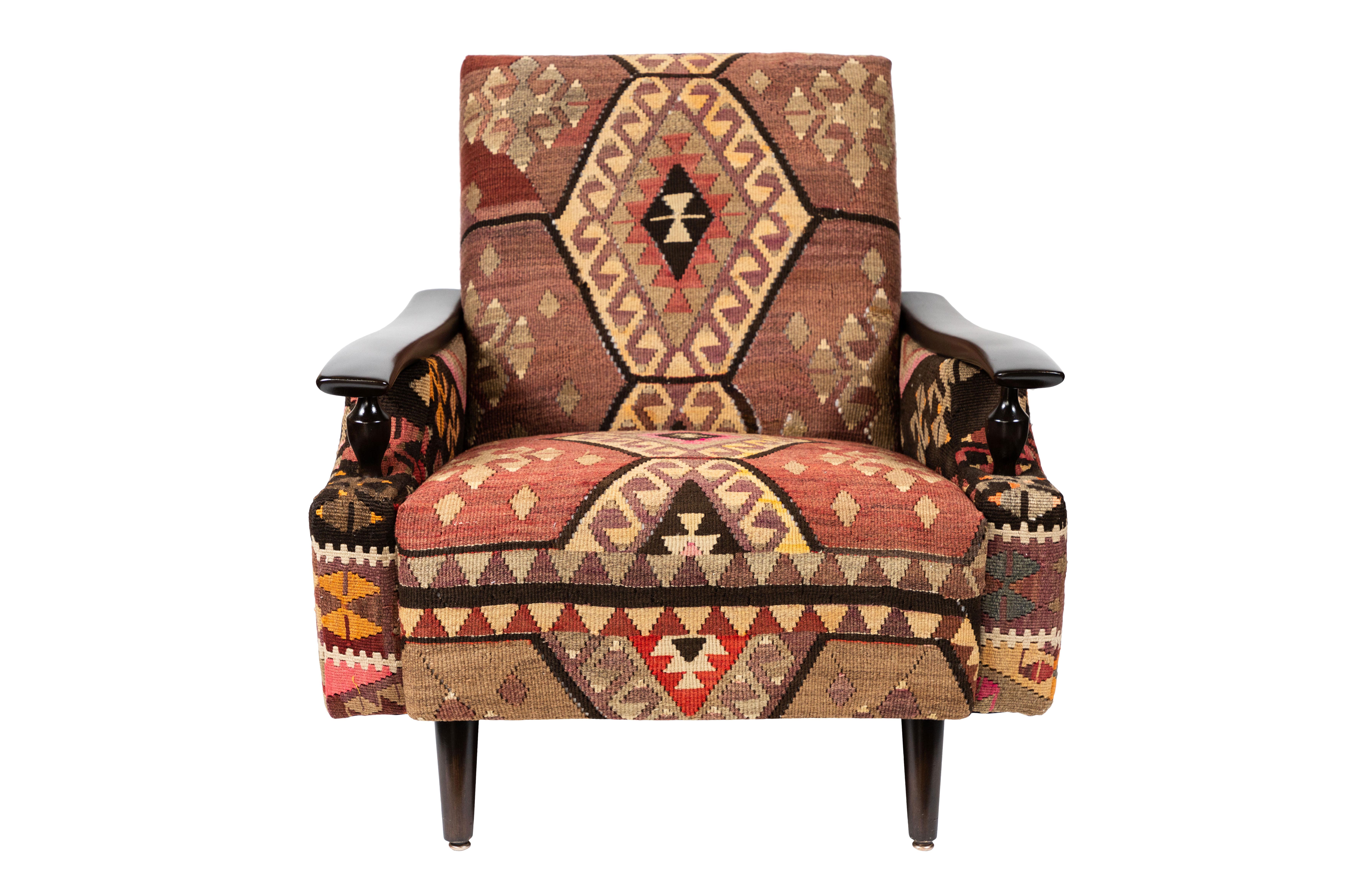 The placement of the pattern elements of this colorful vintage kilim rug make this lounge chair an eye-catcher, whether it's the highlight of a room, or a supporting player in your decor. Wooden elements, curving arms and turned decorative spindles