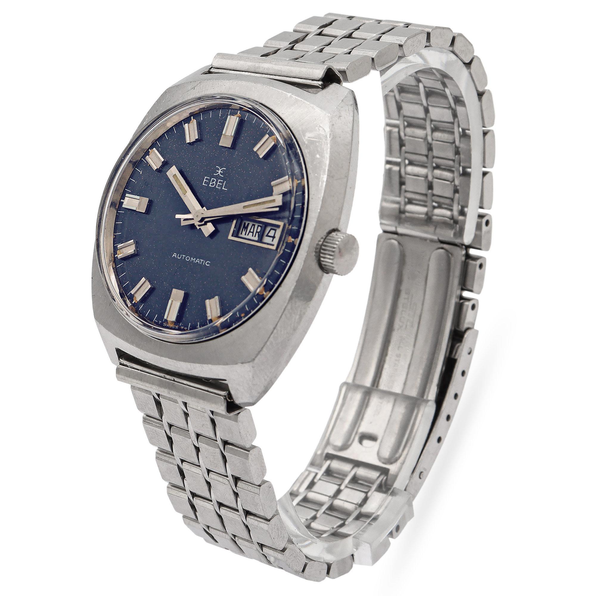 Il s'agit d'une montre-bracelet automatique Ebel vintage, présentant un style classique des années 1970 avec un boîtier en acier inoxydable de forme coussin distinctif et un cadran bleu nuit profond. La montre présente des index appliqués de couleur