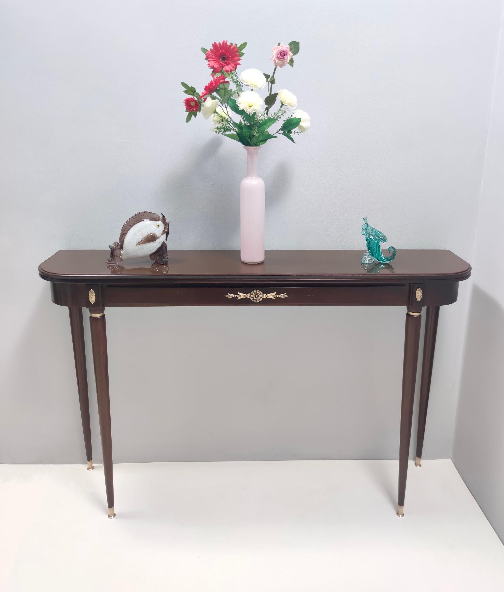 Made in Italy, 1950s.
This console table features an ebonized beech frame, a back-painted glass top and brass details and feet caps. 
It is a vintage piece, therefore it might show slight traces of use, but it can be considered as in excellent