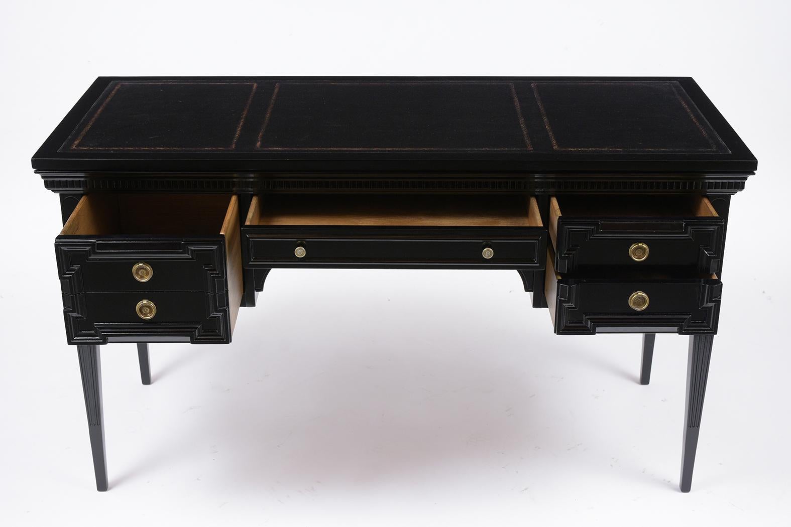This Vintage Louis XVI Style Desk has been professionally restored and has been newly stained in black color with a lacquered finish. This desk features a black color faux leather top with embossed gilt garland pattern details, center drawer with