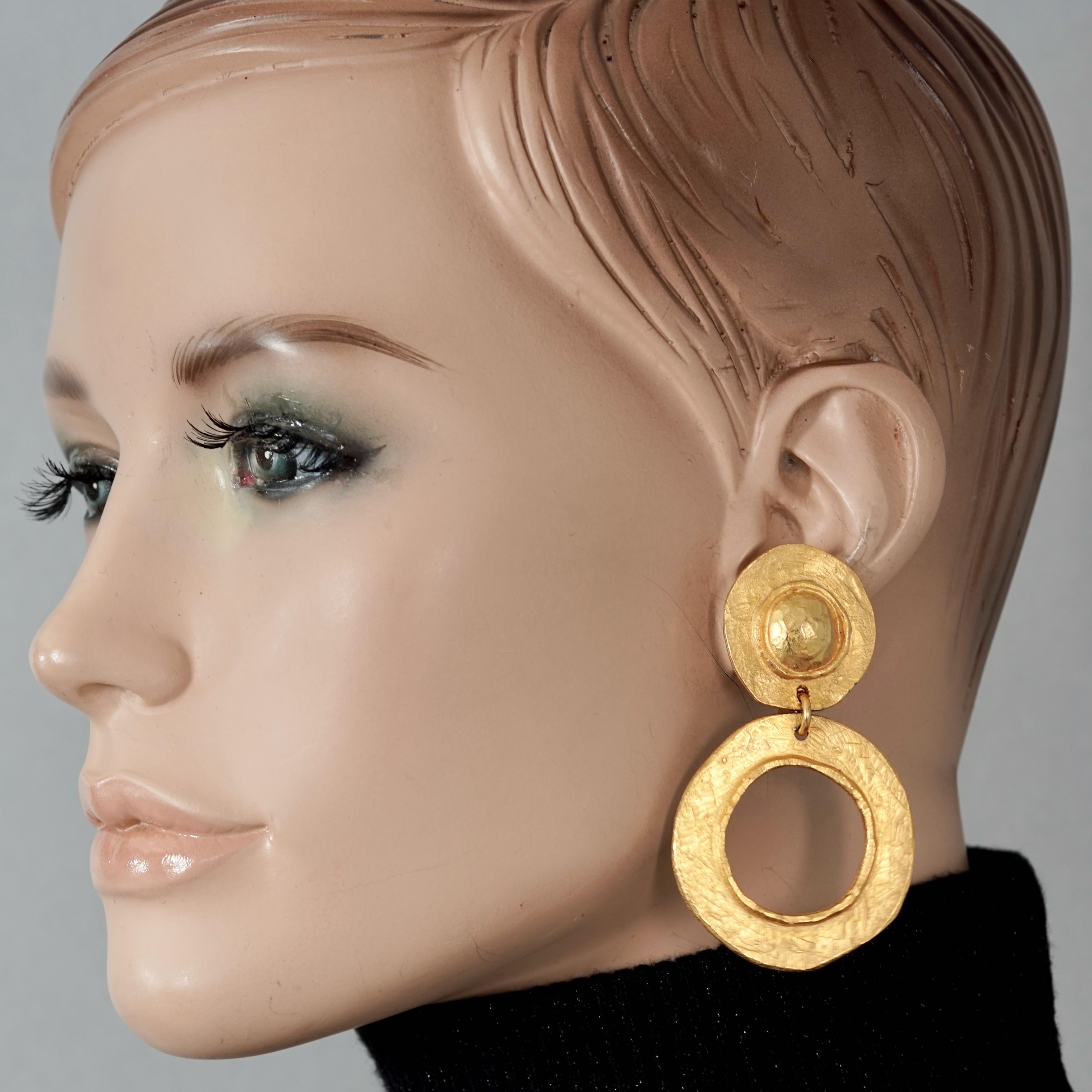 Vintage EDOUARD RAMBAUD Disc Hoop Dangling Earrings

Measurements:
Height: 2.75 inches (7 cm)
Width: 1.57 inches (4 cm)
Weight per Earring: 15 grams

Features:
- 100% Authentic EDOUARD RAMBAUD.
- Hammered disc hoop dangling earrings.
- Gold tone