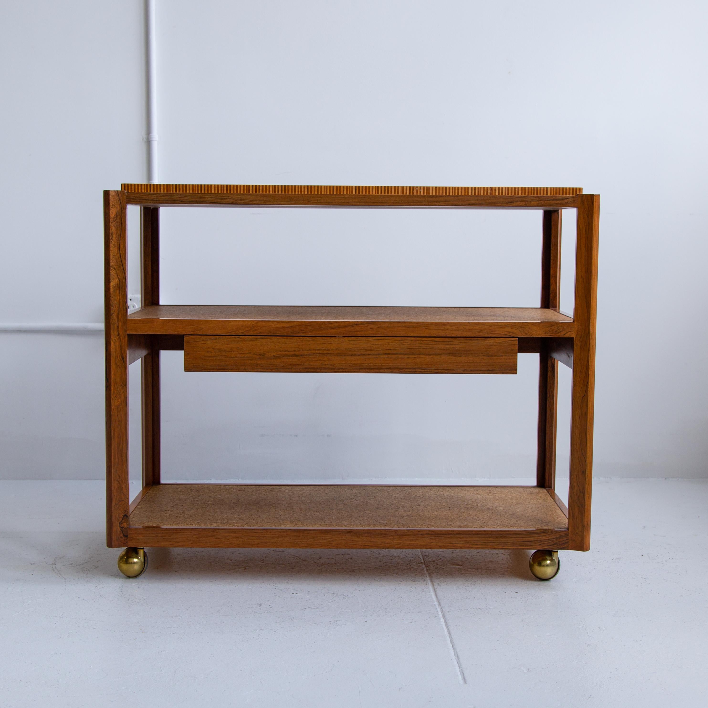 Iconic Edward Wormley for Dunbar serving bar cart or bar trolley with drawer on brass casters. The cart is exquisitely made with a mix extraordinary materials; sculpted Brazilian rosewood frame, shelves are cork covered, and top is laminated