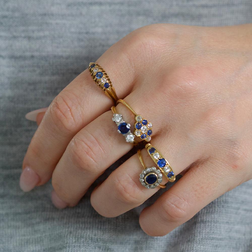 Unser antiker edwardianischer Edelsteinring besticht durch einen ovalen blauen Saphir, den Geburtsstein des Monats September, der Weisheit, Tugend und Glück symbolisiert. Der Saphir ist anmutig von einem Halo aus funkelnden Diamanten umgeben, dem