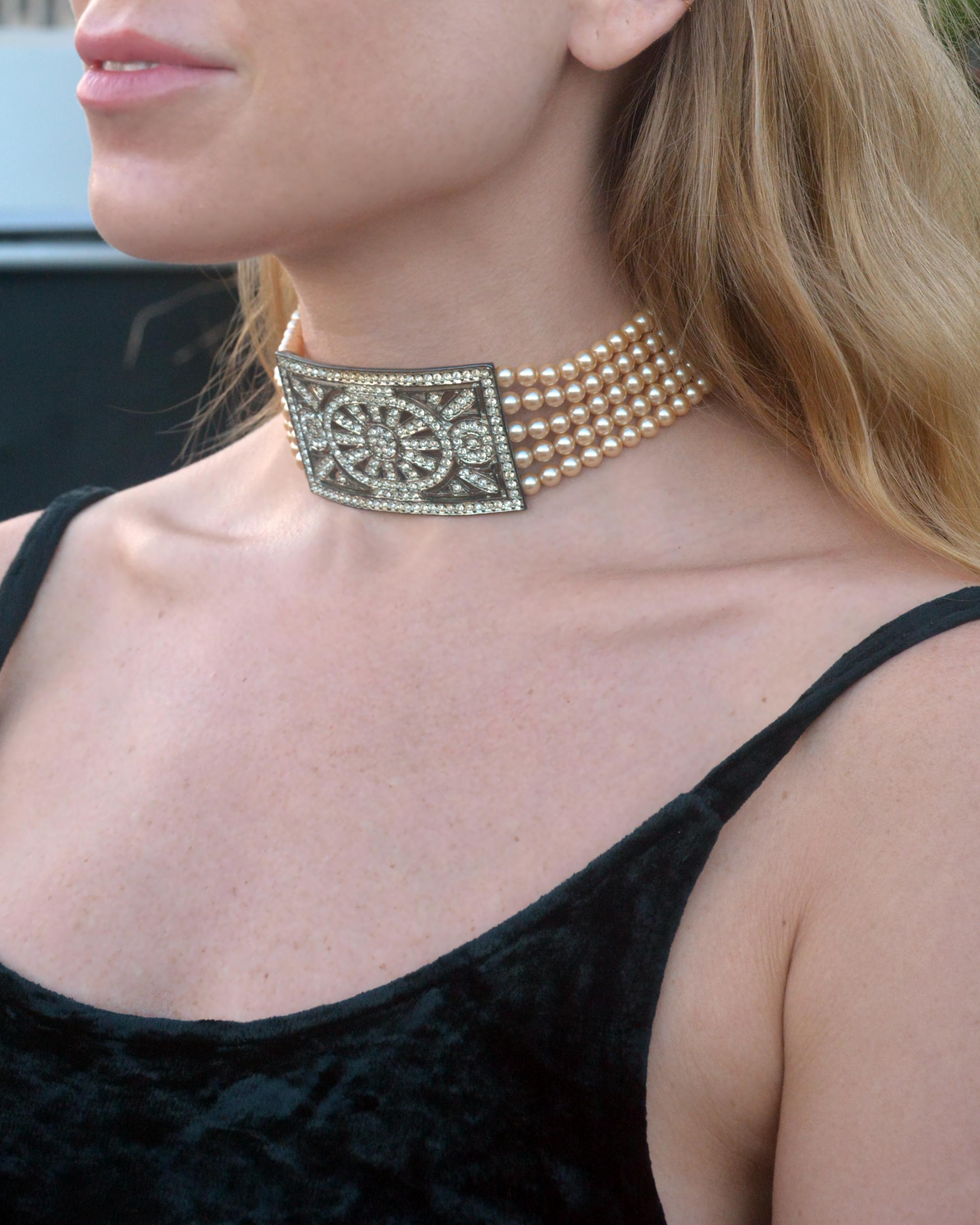 This vintage pearl collar choker draws clear inspiration from antique collar choker styles popular in the Edwardian era. Its five strands of pearls center upon an ornate crystal centerpiece, set in metal with an antique 