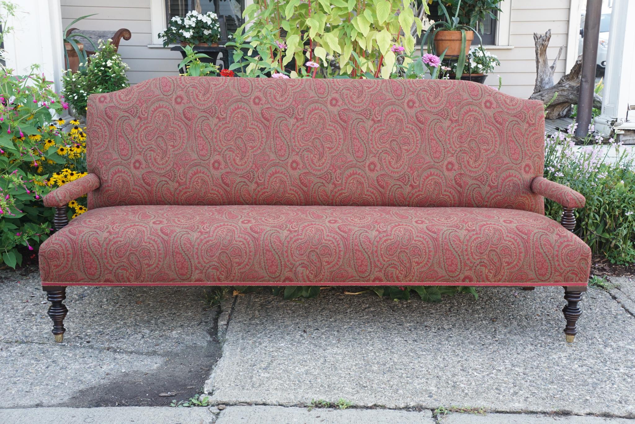 Este gran sofá vintage de estilo eduardiano, fabricado en el siglo XX, está hecho de caoba y tiene los brazos torneados con anillas y las patas delanteras a juego, rematadas en grandes sabots de latón. El respaldo alto y el asiento profundo