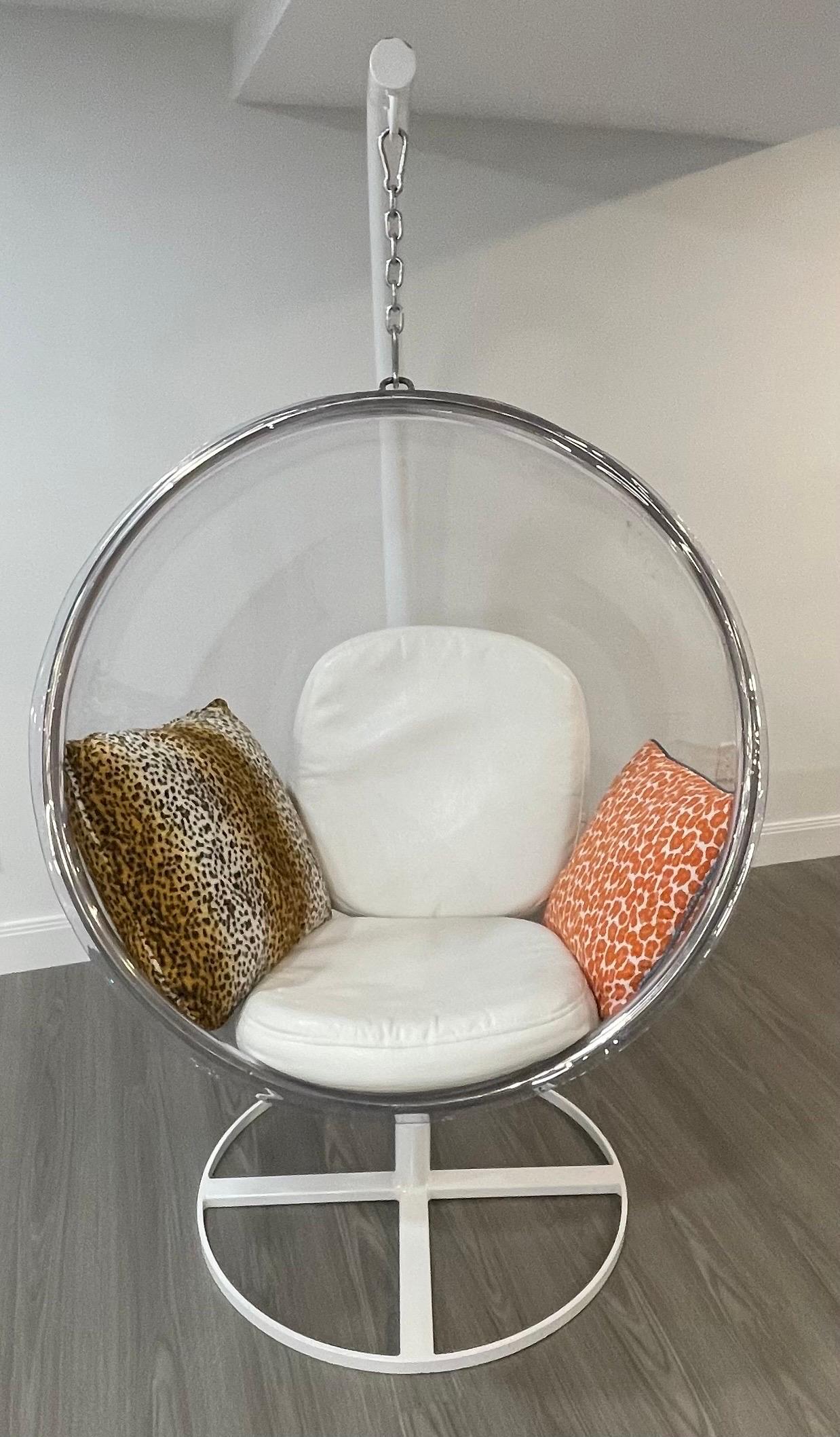 Une merveilleuse chaise bulle suspendue en Lucite / Acrylique de style Eero Aarnio avec un support enduit de poudre blanche, accompagnée de coussins en faux cuir blanc pour l'assise et le dossier et de deux coussins décoratifs à motif