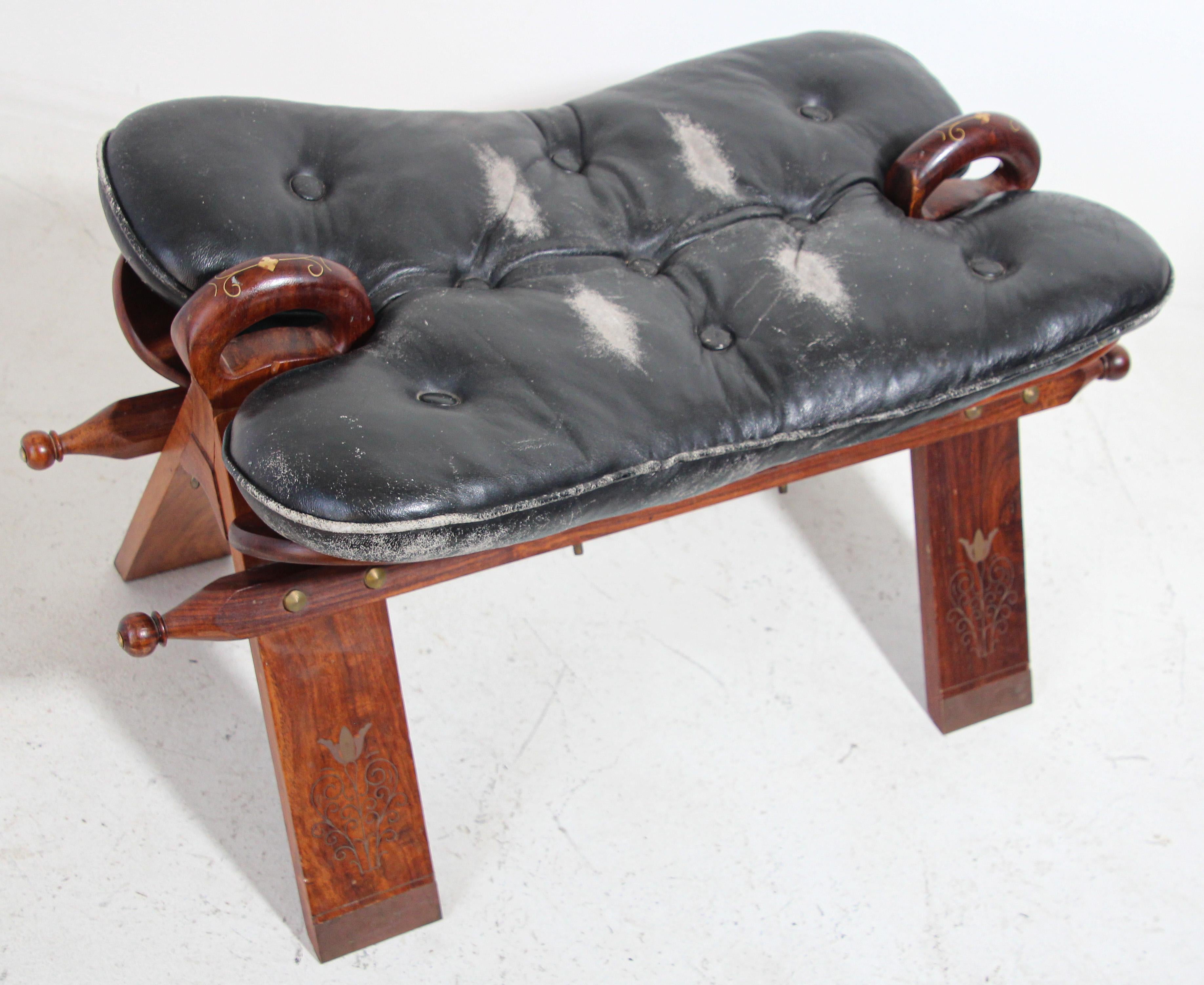 Vintage Egyptian, North Africa camel saddle shape stool.
A middle eastern wood and leather camel saddle wood bench designed with a wooden frame and a black button tufted leather cushion seat.

Traditionally used to ride camels in the desert of
