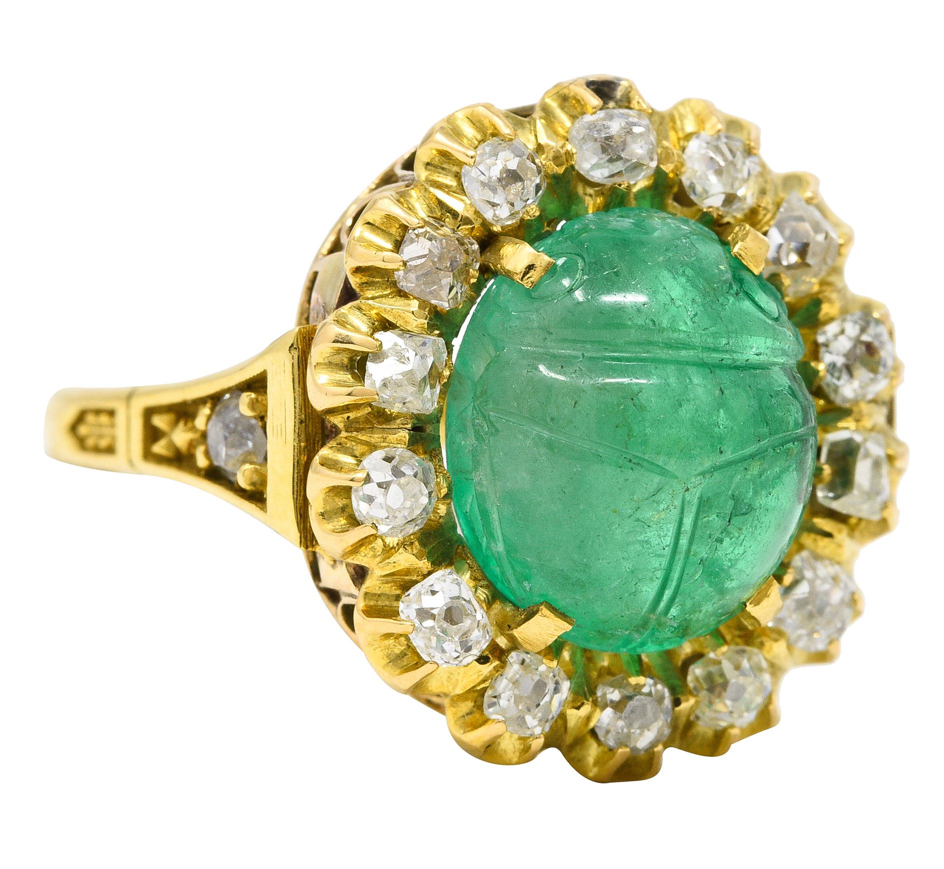 Featuring an antique circular cluster atop vintage cathedral shoulders. Centering an oval emerald cabochon weighing approximately 6.80 carats - bluish green. Deeply carved as a scarab motif and semi-transparent with natural inclusions - some surface