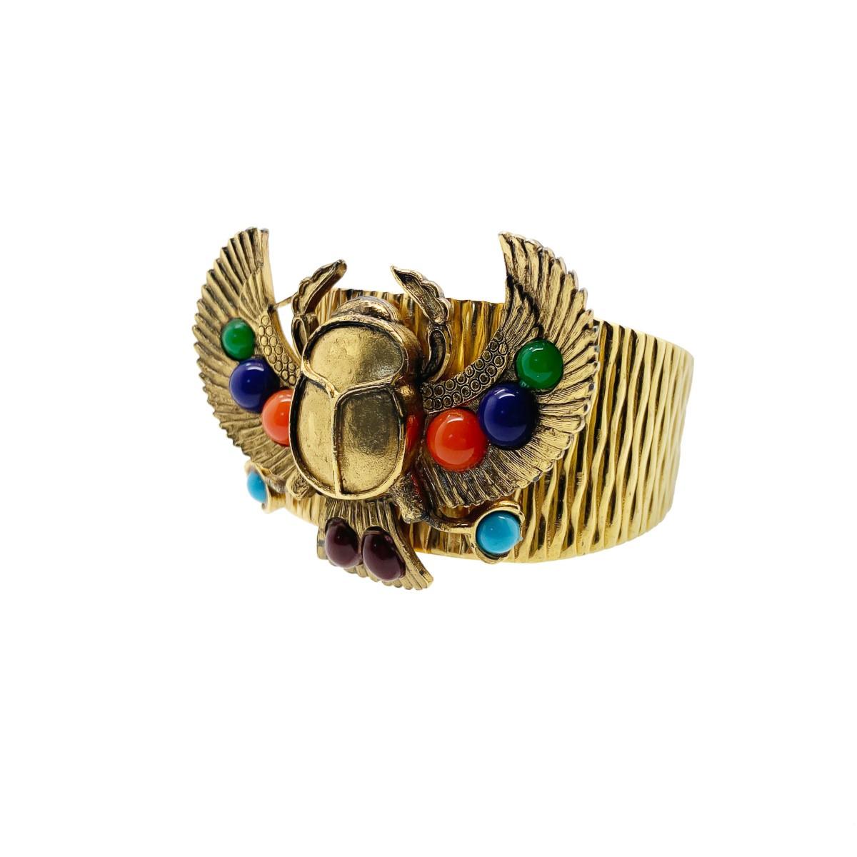 A stunning Vintage Egyptian Revival Scarab Cuff. Featuring a bark effect cuff with large Egyptian stylised scarab plaque set with coloured glass cabochons. 
Vintage Condition: Very good without damage or noteworthy wear. 
Materials: Gold plated