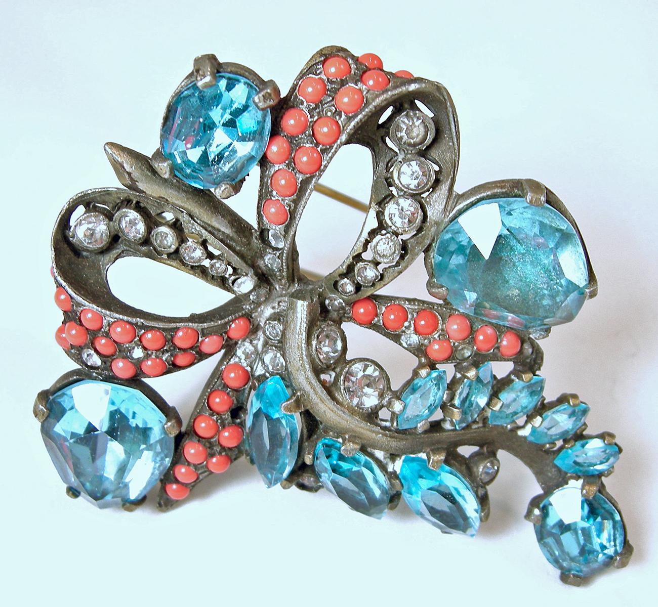 Although this vintage Eisenberg fur clip is not signed … there is no doubt this is an Eisenberg as it is a well-recognized piece.  It has faux coral beads and clear crystals in a ribbon design.  Multi shaped blue crystals makes this fur clip