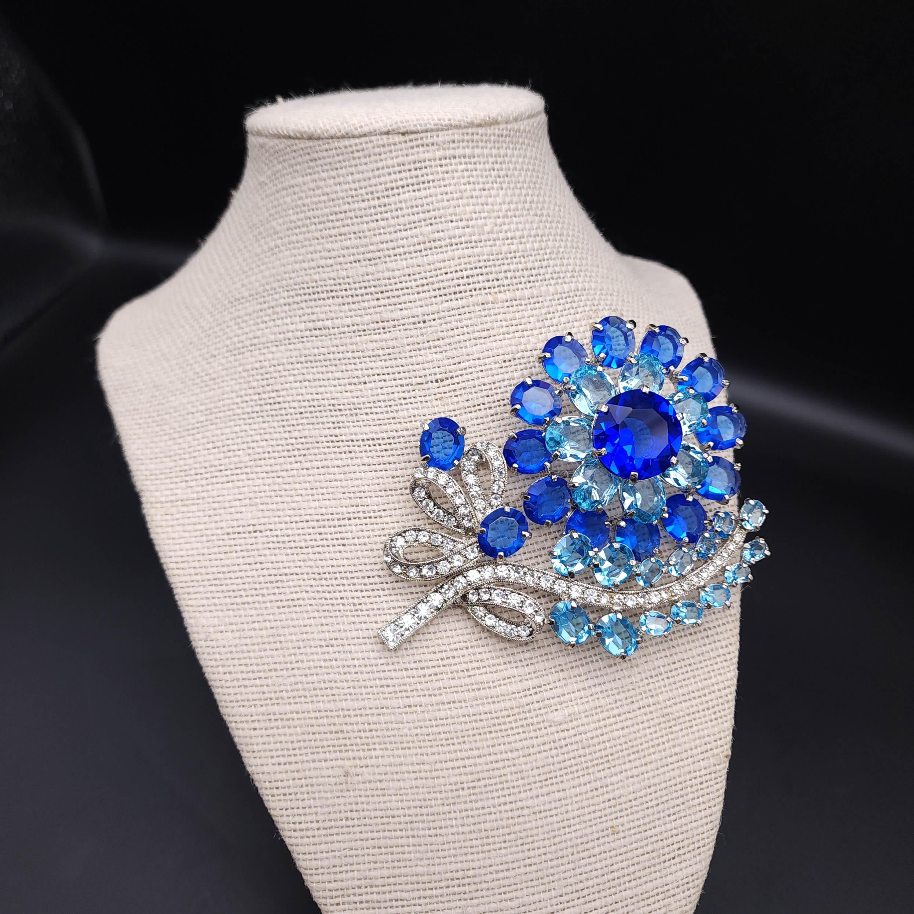 Elevate your ensemble with the timeless elegance of this vintage Eisenberg Ice pin! 

Crafted in a radiant silver tone, this exquisite brooch showcases a dazzling flower adorned with large prong-set sapphire and aquamarine crystals that capture the