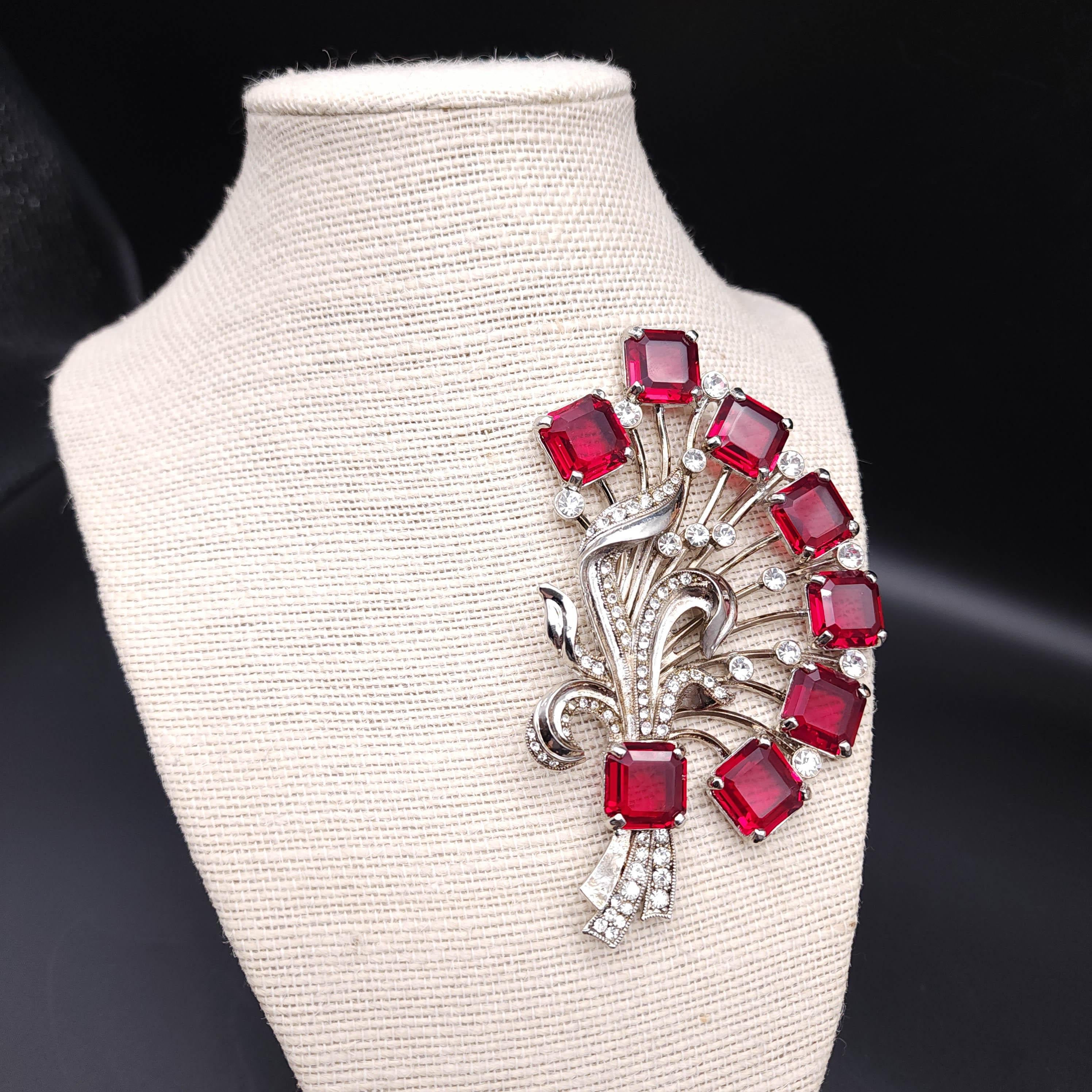 Discover the charm of yesteryear with this Vintage Eisenberg Ice flower bouquet pin brooch. This exquisite piece features a timeless silver design, with each flower meticulously adorned with prong-set ruby crystals that exude a rich, vibrant hue.