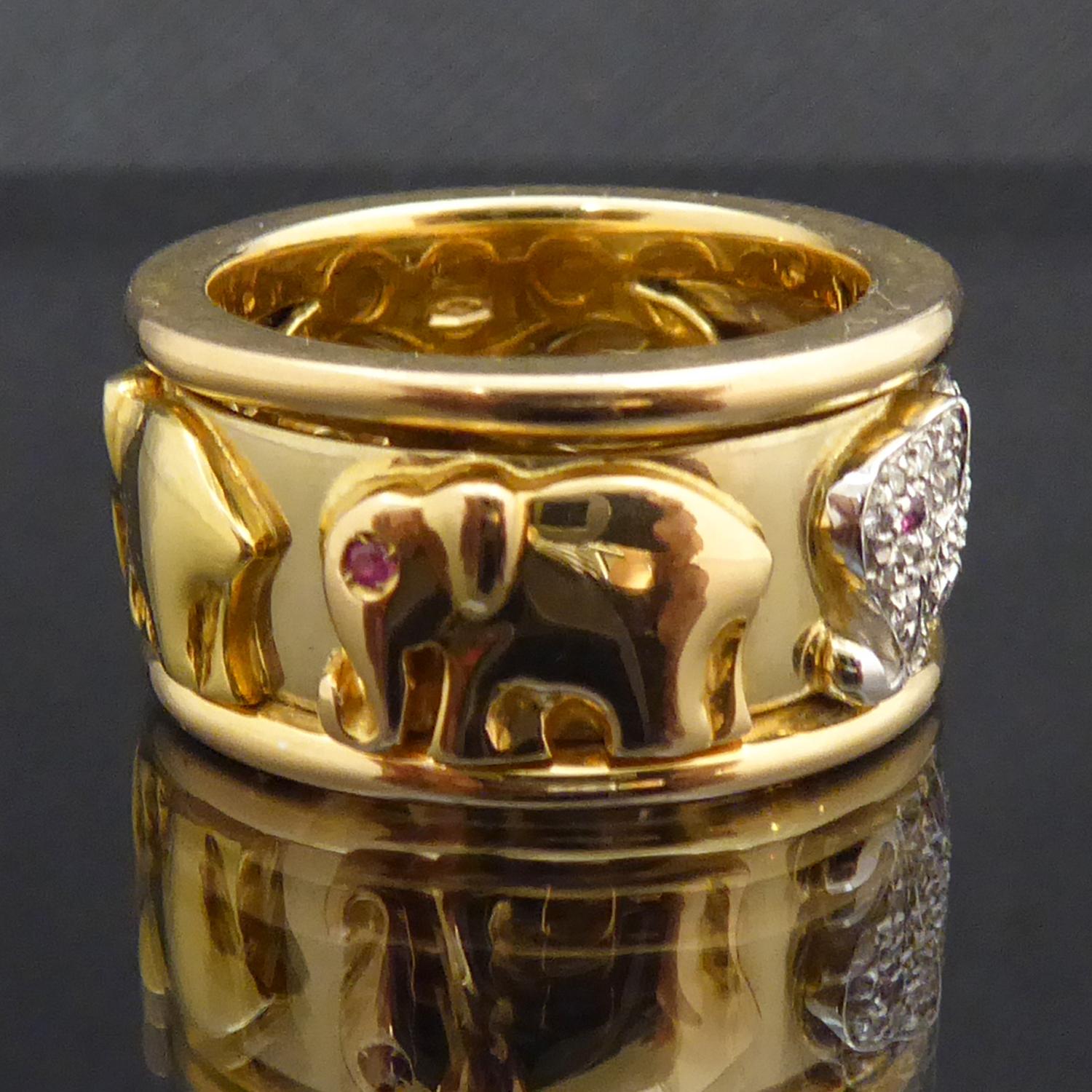 A thoroughly delightful gold band depicting a herd of elephants in their characteristic trunk-to-tail elephant walk.  The ring features five gold elephants, each set with a ruby eye walking around the centre of the gold band.  One of the elephants,