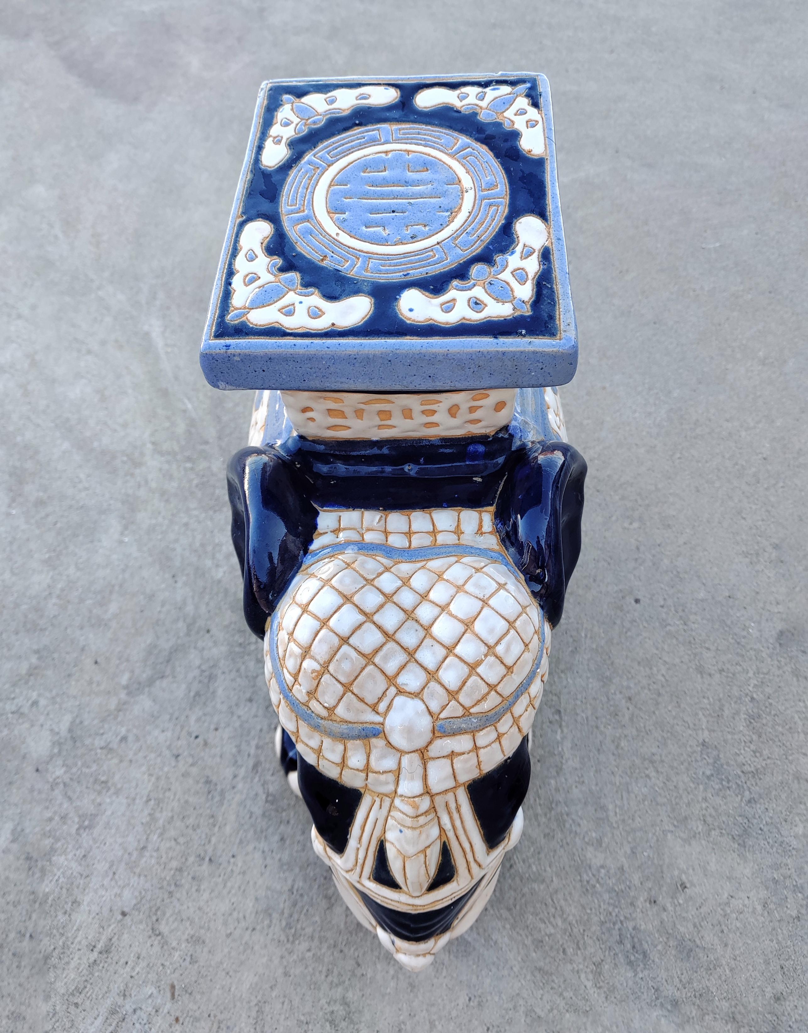 In this listing you will find a large ceramic and very decorative garden stool or plant stand in the shape of an elephant made in blue and white ceramics. A saddle seat and blanket on the elephant are glazed with celadon hues, laced with cobalt blue
