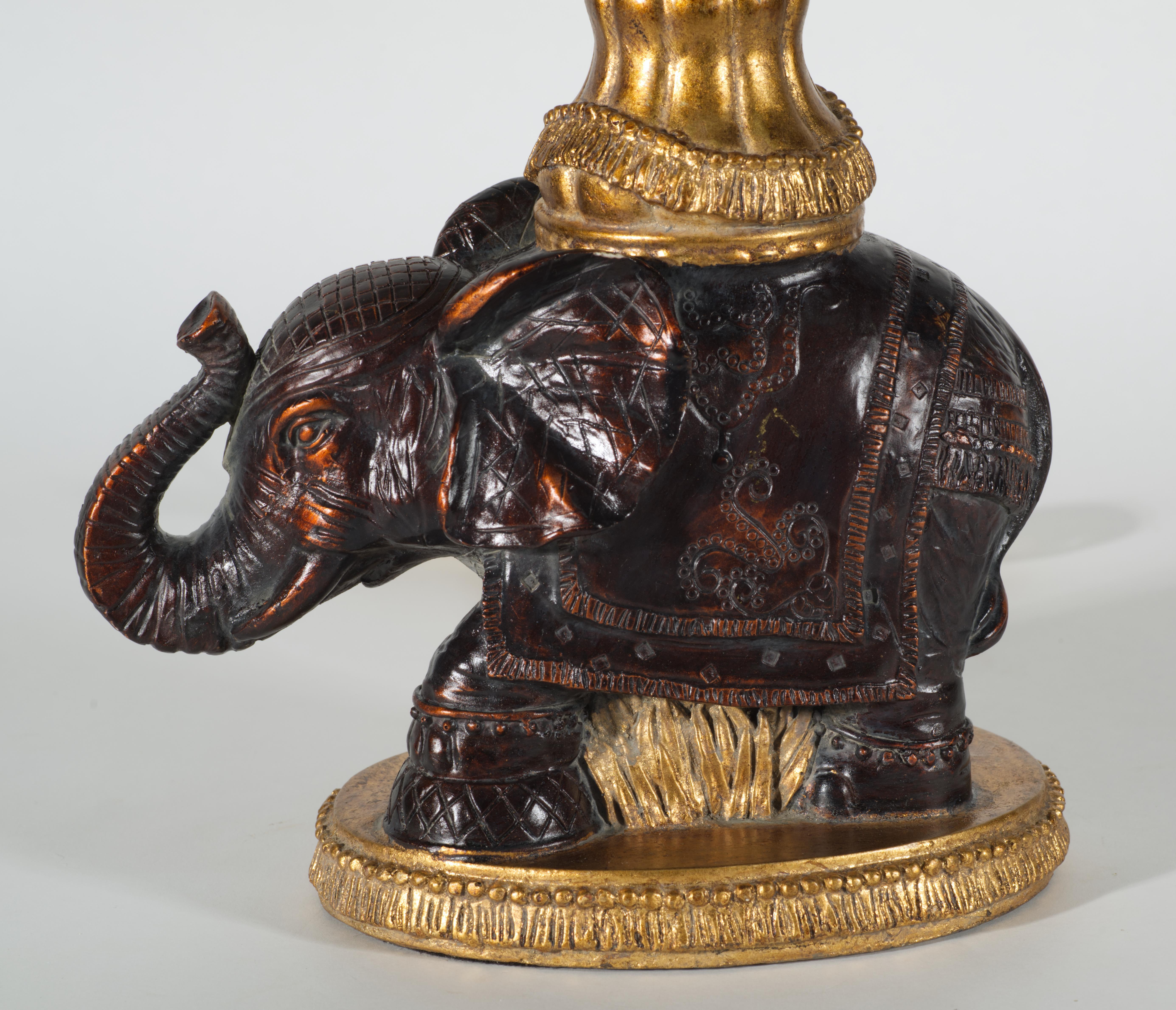  Vintage table or accent lamp features an elephant standing on the oval base with its trunk lifted up while holding a baluster or candlestick shaped column. The lamp is sculpted with great attention to detail; the elephant's gear and the baluster
