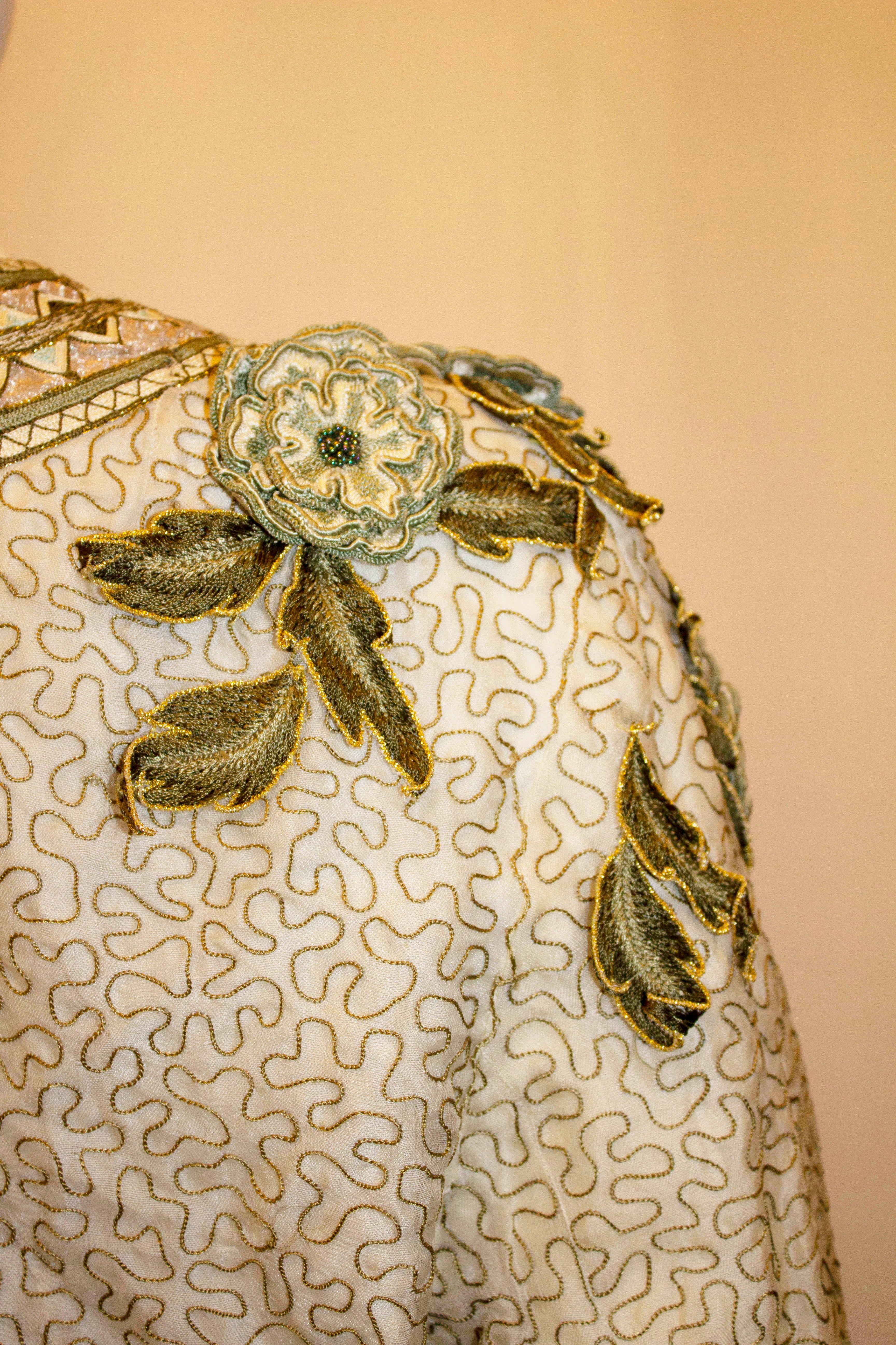 Une superbe veste en soie vintage par Ella Saint. La veste a un fond ivoire  avec une encolure ronde avec des détails en applique,  et un motif sur le bord et les poignets. Les couleurs prédominantes sont l'or  et vert.  Mesures : Poitrine jusqu'à t