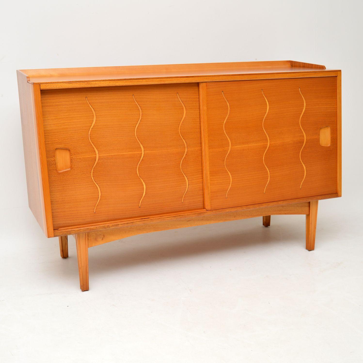 A stunning and very unusual vintage elm and walnut sideboard by Ian Audley for GW Evans. This was made in England, it dates from the 1950’s.

It has has a walnut carcass, elm sliding doors and lovely grooved etched patterns in a half helix design on