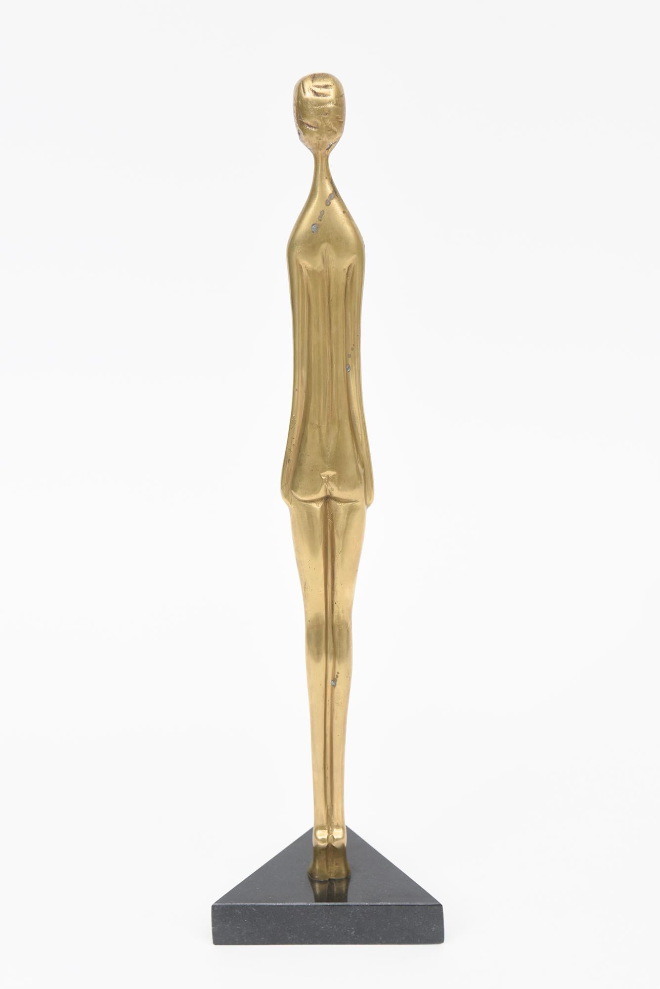 Questa scultura figurativa femminile allungata d'epoca, alta e sottile, poggia su una base triangolare in granito.  L'altezza della sola scultura in ottone è di 14