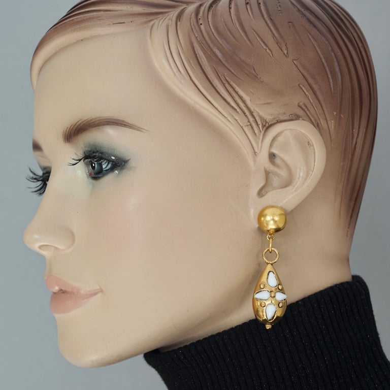 Vintage EMANUEL UNGARO White Flower Cabochon Dangling Earrings

Measurements:
Height: 2.36 inches (6 cm)
Width: 0.62 inch (1.6 cm)
Weight per Earring: 10 grams

Features:
- 100% Authentic EMANUEL UNGARO.
- White flower cabochon dangling earrings.
-