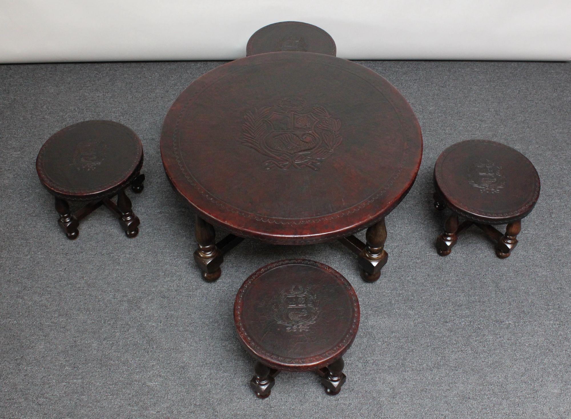Embossed leather and stained mahogany coffee/cocktail table and four nesting stools depicting the Peruvian coat of arms since 1825 and embellished with tooled 'wave' border pattern (ca. 1950, Peru). The coat of arms features a shield bearing a