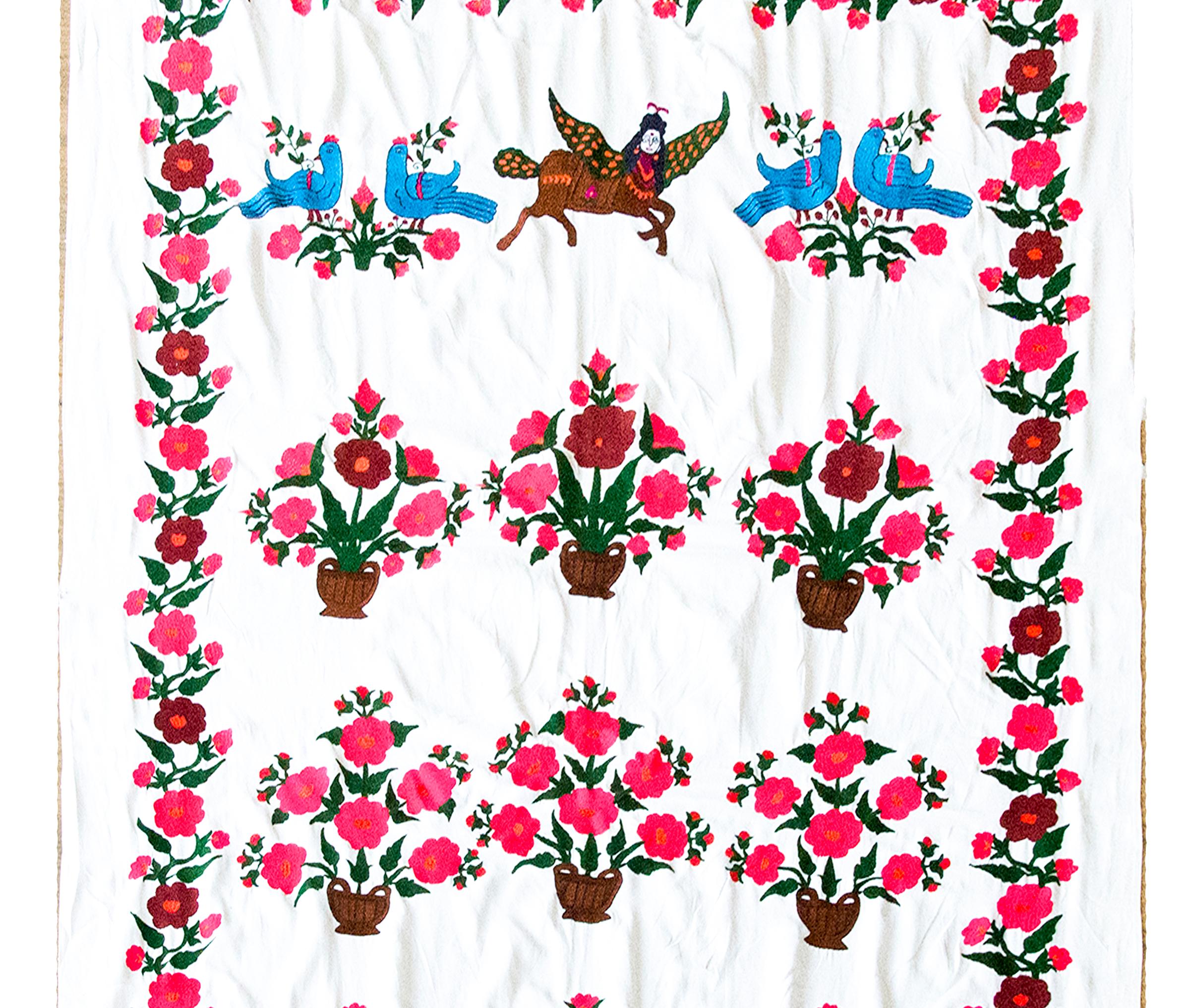 This vintage late 20th-century Suzani textile bursts with color, symbolism, and intricate craftsmanship. Hand-embroidered medallions depict baskets brimming with large-scale flowers and buds, rendered in bright pinks and soft greens, celebrating