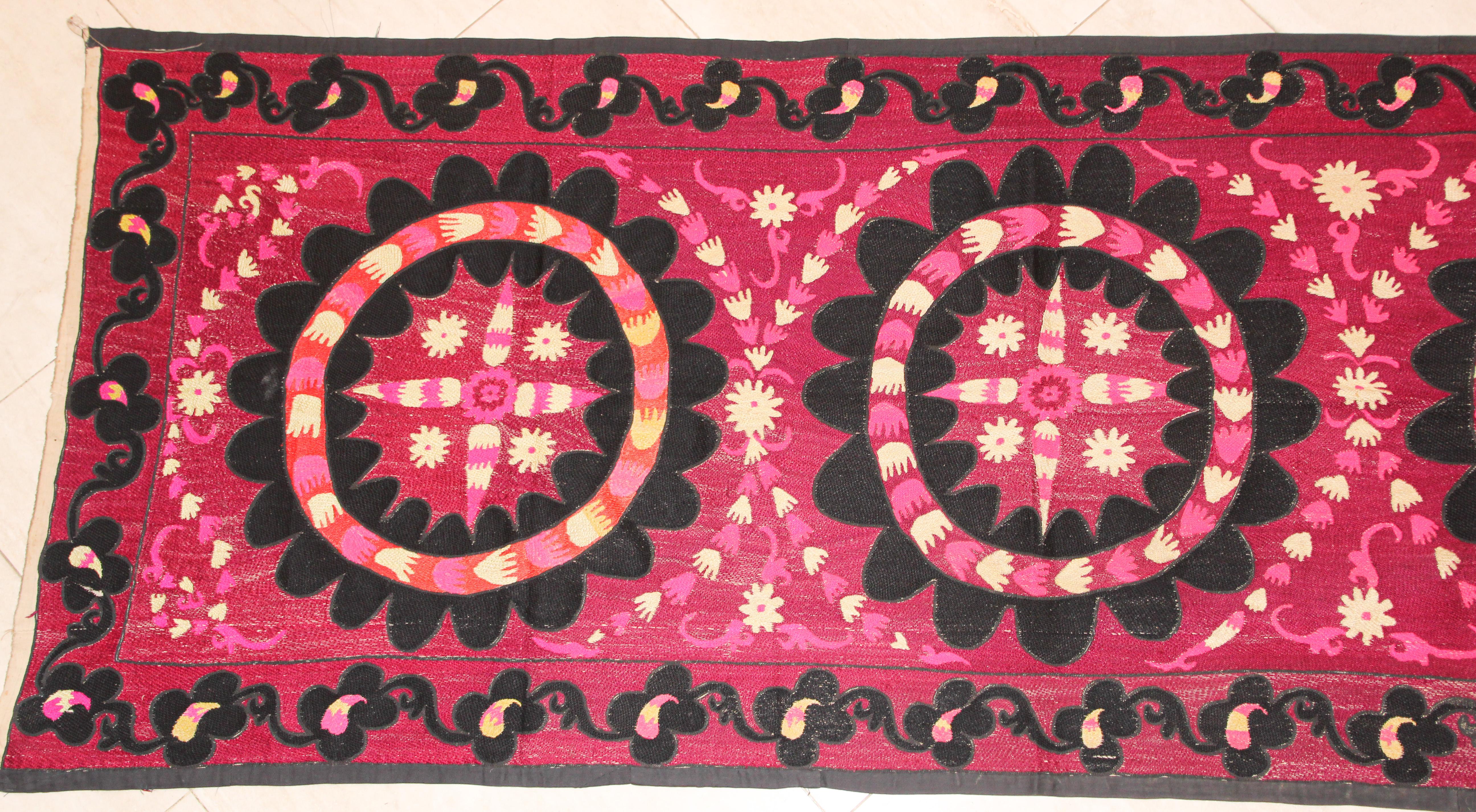 Vintage embroidered Uzbek Suzani.
Beautiful suzani hand-stitched Turkish designs with silk in traditional patterns and vibrant pink, fuschia pink, purple black colors and off white beige.
The suzani features a row of three medallions flowers within