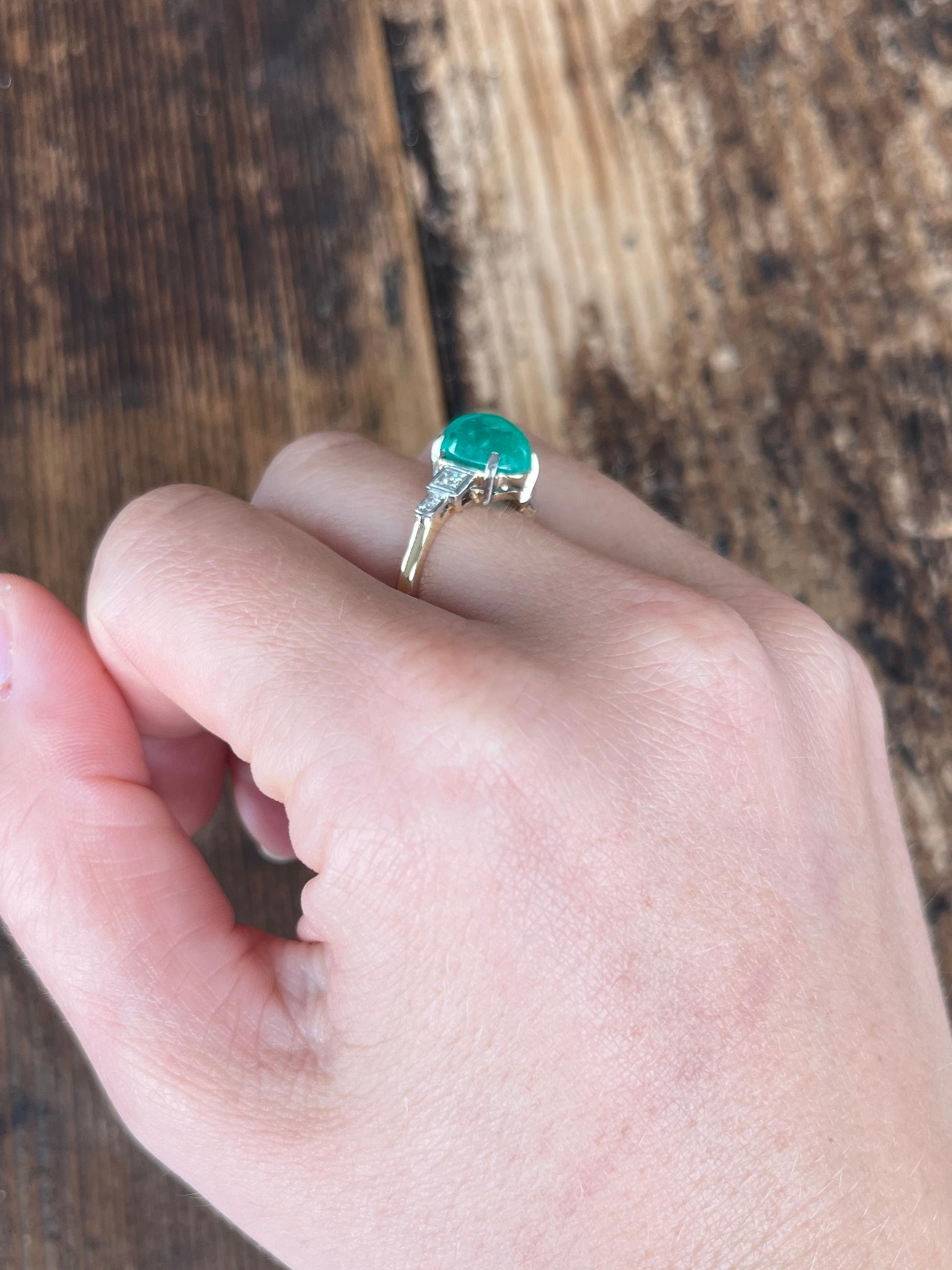 This stunning stone is a cabochon emerald and is so striking! Either side of the glossy bright green stone are two sparkling diamonds set within the platinum step shoulders. The diamond shoulders total 5pts each. 

Ring Size: O or 7 1/4
Height Off