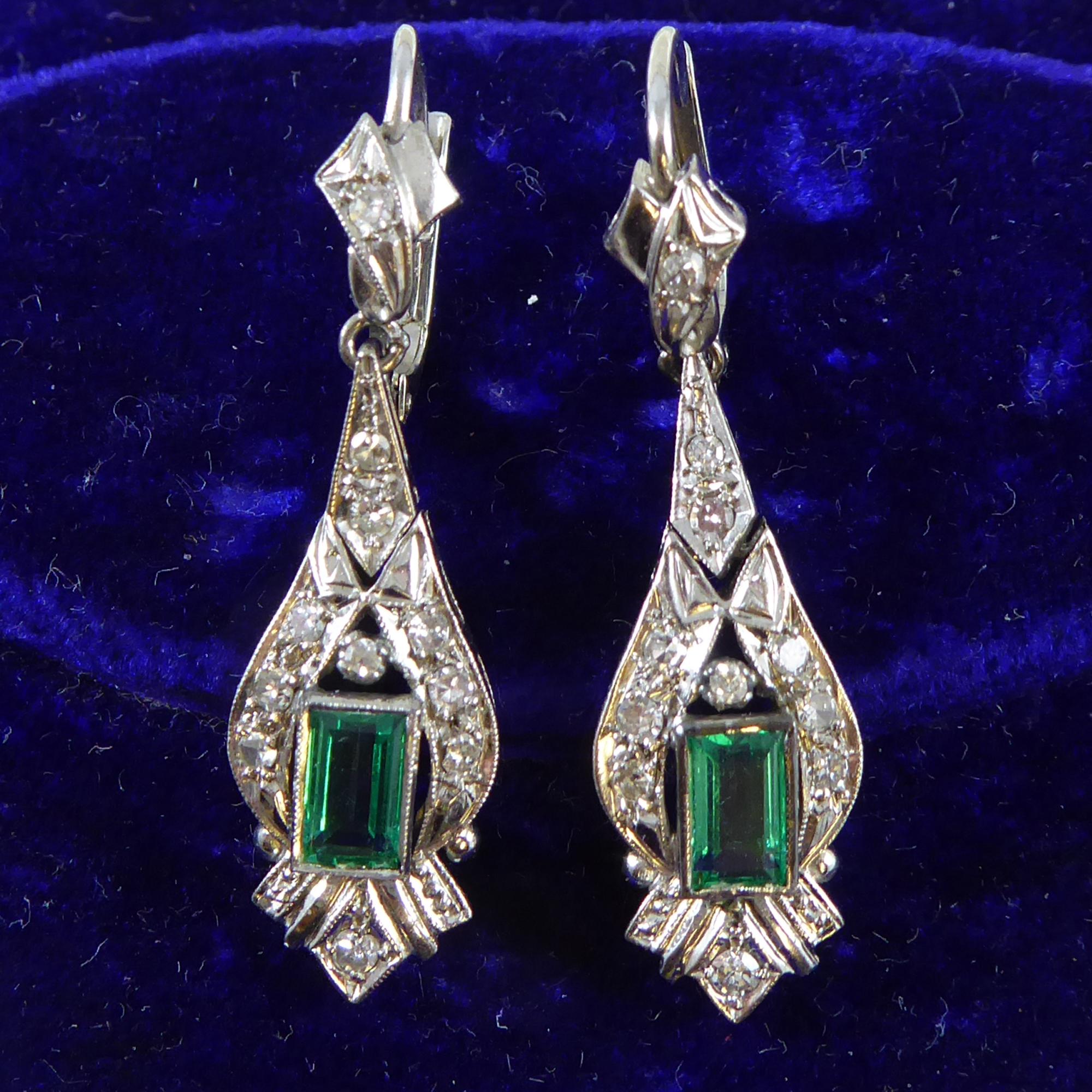 Dating from the 1950s these lavish emerald and diamond drop earrings will add a touch of glamour to the most deluxe evening event.  Each earring consists of a millegrain set, rectangular trap cut, medium-coloured emerald of good clarity.  Both