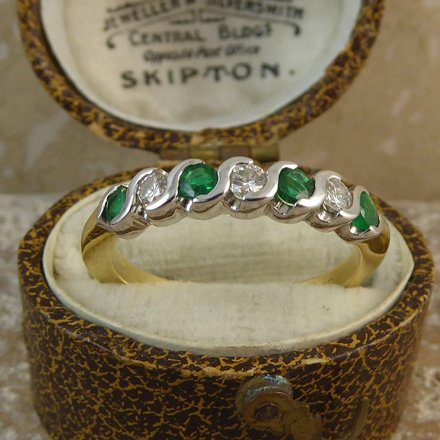 A minimalist style vintage eternity ring half set with alternating emeralds and diamonds and having a total of four emeralds and three diamonds, each approx. 3.0mm in diameter.  The gemstones are set in white gold S-shaped rub-over mounts to a