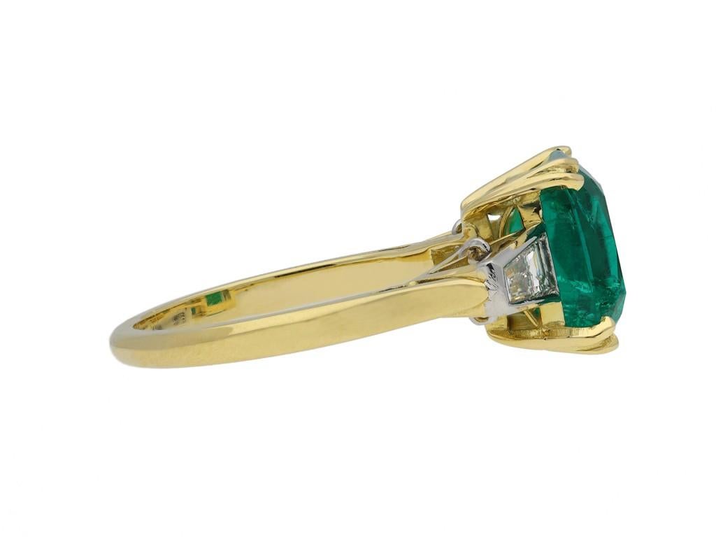 Colombian emerald and diamond ring. Centrally set with a rectangular old cut natural Colombian emerald with no colour enhancement and minor clarity enhancement in an open back split corner claw setting with an approximate weight of 3.11 carats,